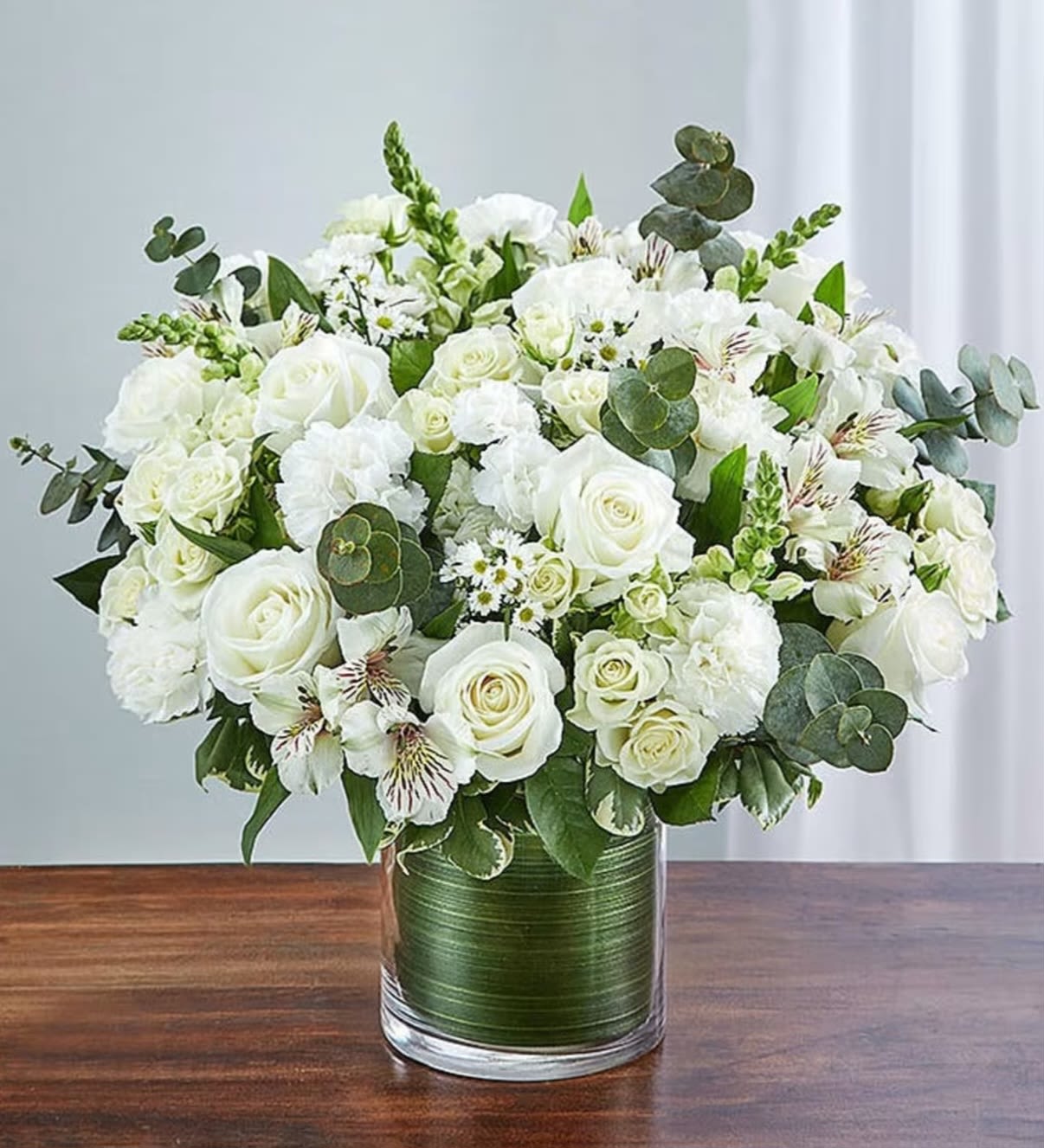 New Beginnings - New beginnings deserve flowers! This arrangement is full of the freshest all white blooms with accents of fragrant eucalyptus and other seasonal white This classic bouquet is the perfect gift for celebrating a new year, a new baby, or a newly married couple. Arranged compact and delivered in a green satin ribbon lined glass cylinder vase.   APPROXIMATE DIMENSIONS 13" W X 14" H Orientation: All around