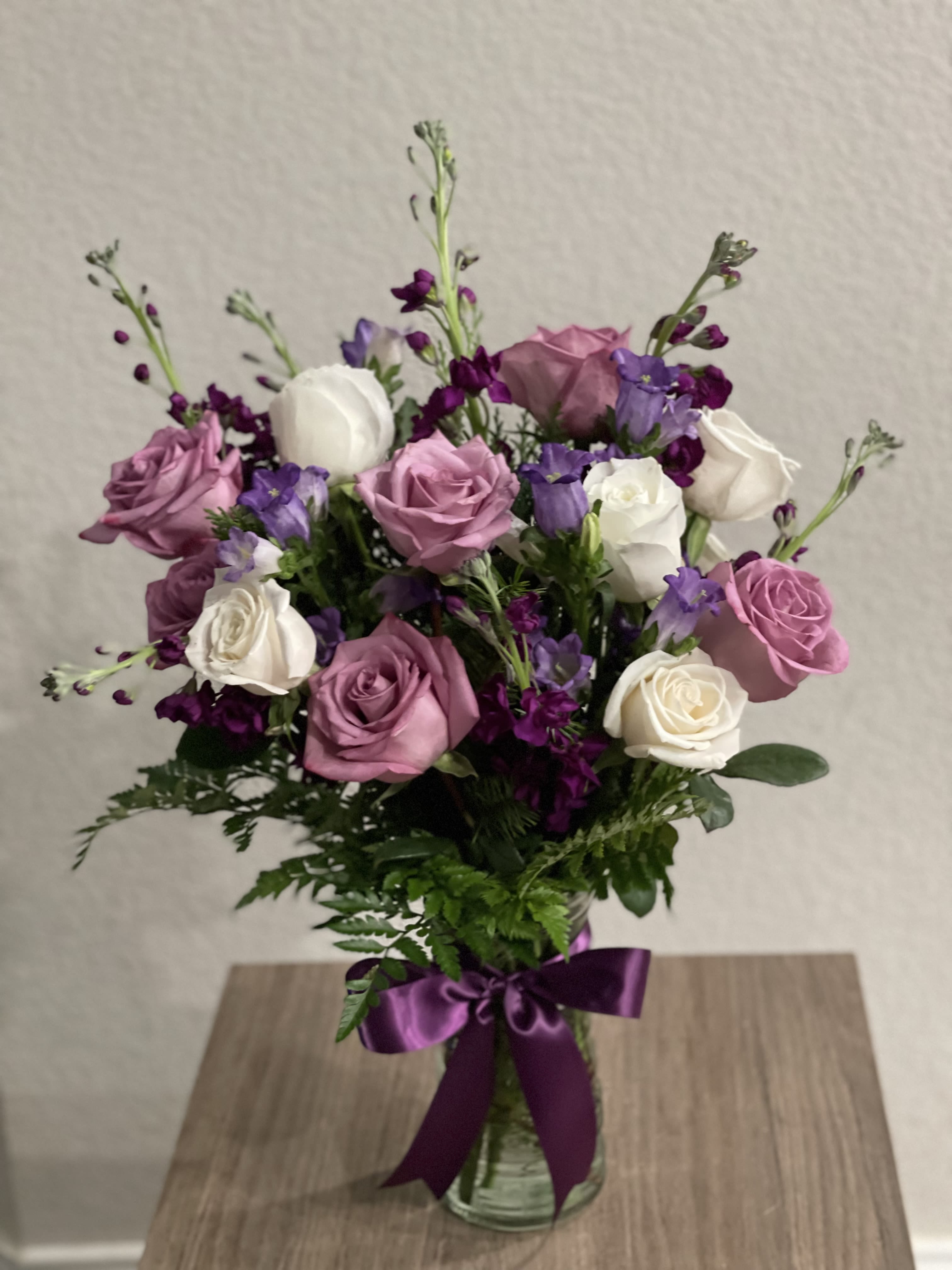 Ladies Day  - Delightful bouquet of white and purple roses, campanula flowers, purple stocks and greens all around on a clear vase with an elegant bow.