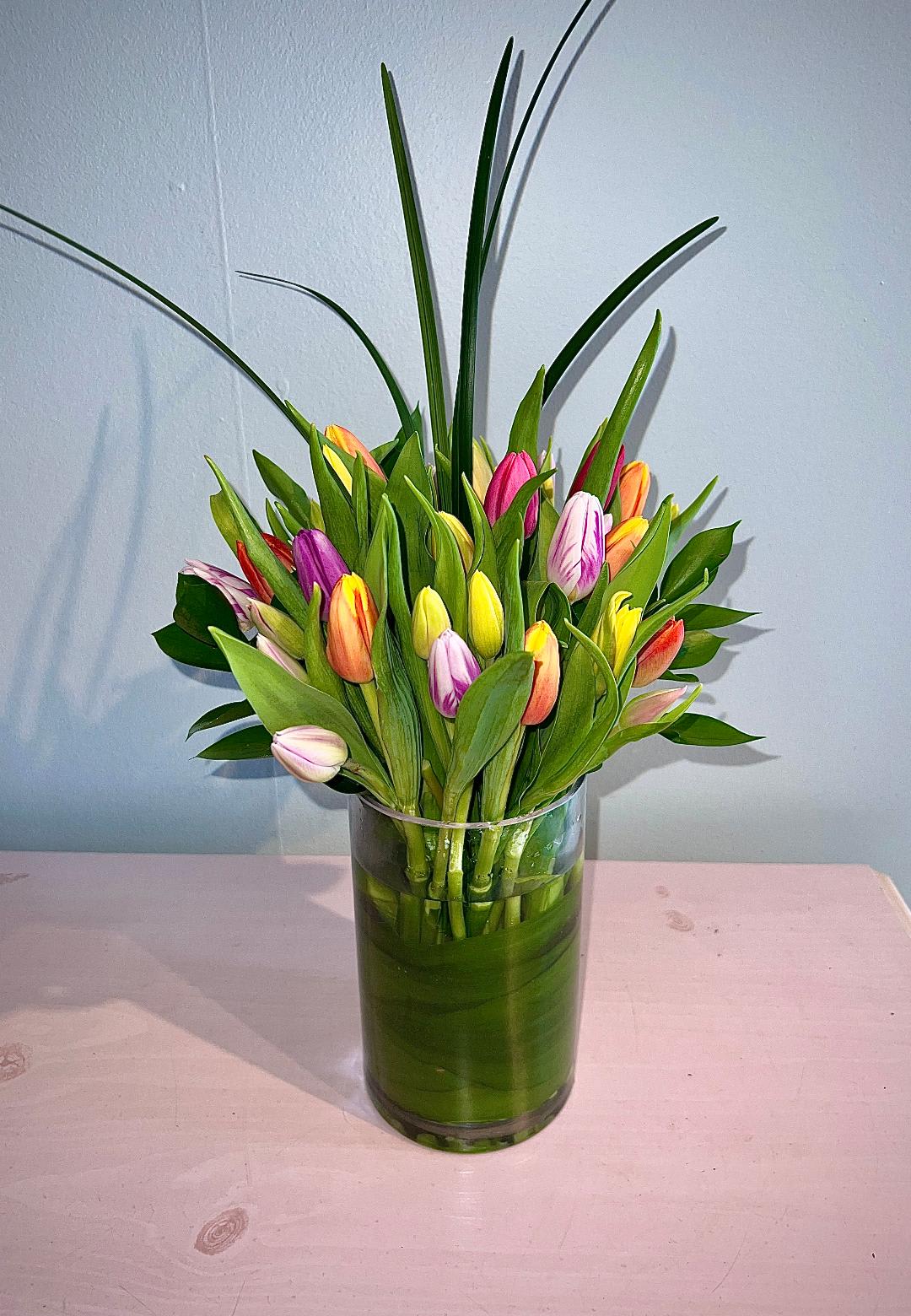 " Two Lips" - 20 beautiful tulips of various colors arranged in an 8" tall glass vase and garnished with Lily Grass and Lemon leaf for that upscale Contemporary look.  Simply Gorgeous!!  Please Note: Florist will do their best to ensure there are at least 3-4 colors of tulips. Color requests can be made in the "Special Instructions" section and we will do our best to accommodate if we have the selections.
