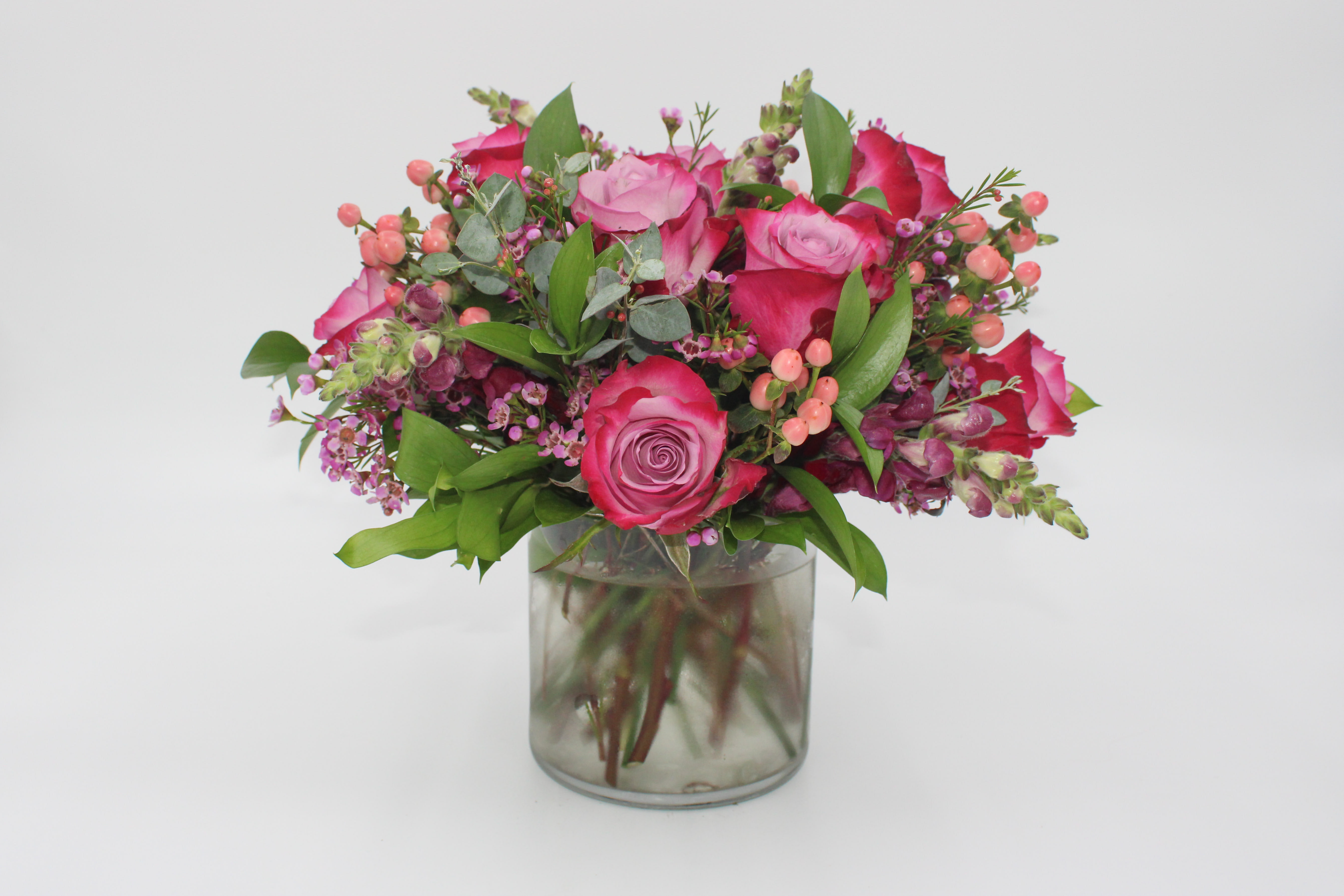 Plume - Plume features Purple Roses, Pink Hypericum Berries, Purple Waxflower, Purple Snapdragon, Italian Ruscus and Gunnii Eucalyptus. Measurements: The Small Plume is designed in a 5x5 inch glass cylinder vase and the Medium Plume is designed in a 6x6 inch glass cylinder vase.
