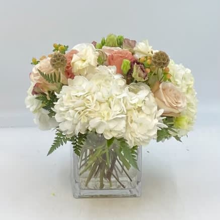 Upstate - Upstate is a gorgeous arrangement of fall neutrals of Quicksand and Moab roses, brown Lisianthus, peach Hypericum Berries, white Ranunculus, pods and more in a clear glass square vase.