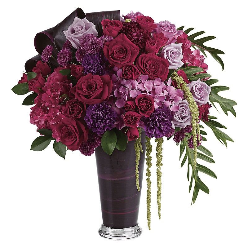 Cascading Elegance Bouquet - A dramatic display in jewel-toned roses and hydrangea in a sophisticated vase, this majestic bouquet will take their breath away. Dark pink hydrangea, lavender hydrangea, lavender roses, light lavender roses, red roses, red spray roses, purple carnations, purple button spray chrysanthemums, and purple cushion spray chrysanthemums are arranged with hanging green amaranthus, israeli ruscus, xanadu philodendron leaves, and red ti leaves. Delivered in a glass romanesque vase.