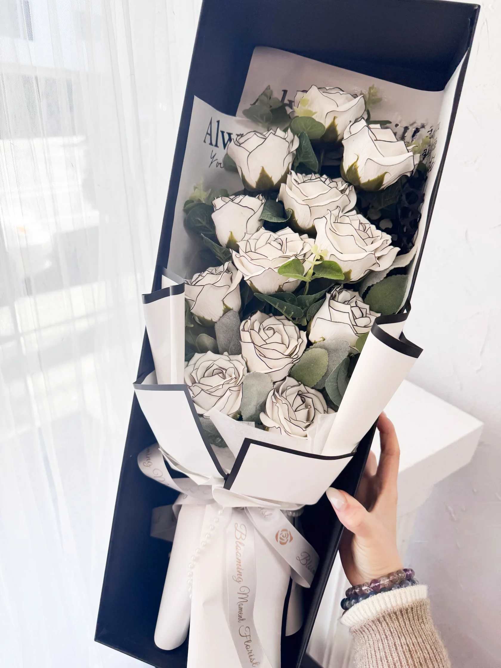 [SOAP FLOWER] Dozen White Liner Soap Rose Bouquet Long Gift Box - Elevate your gifting game with our SOAP FLOWER Dozen White Liner Soap Rose Bouquet. Adorned with 12 premium, large White Liner Roses and paired with the aromatic touch of Eucalyptus, this bouquet is sure to impress. Complete with a sleek black long gift box, it's the perfect present for any occasion.