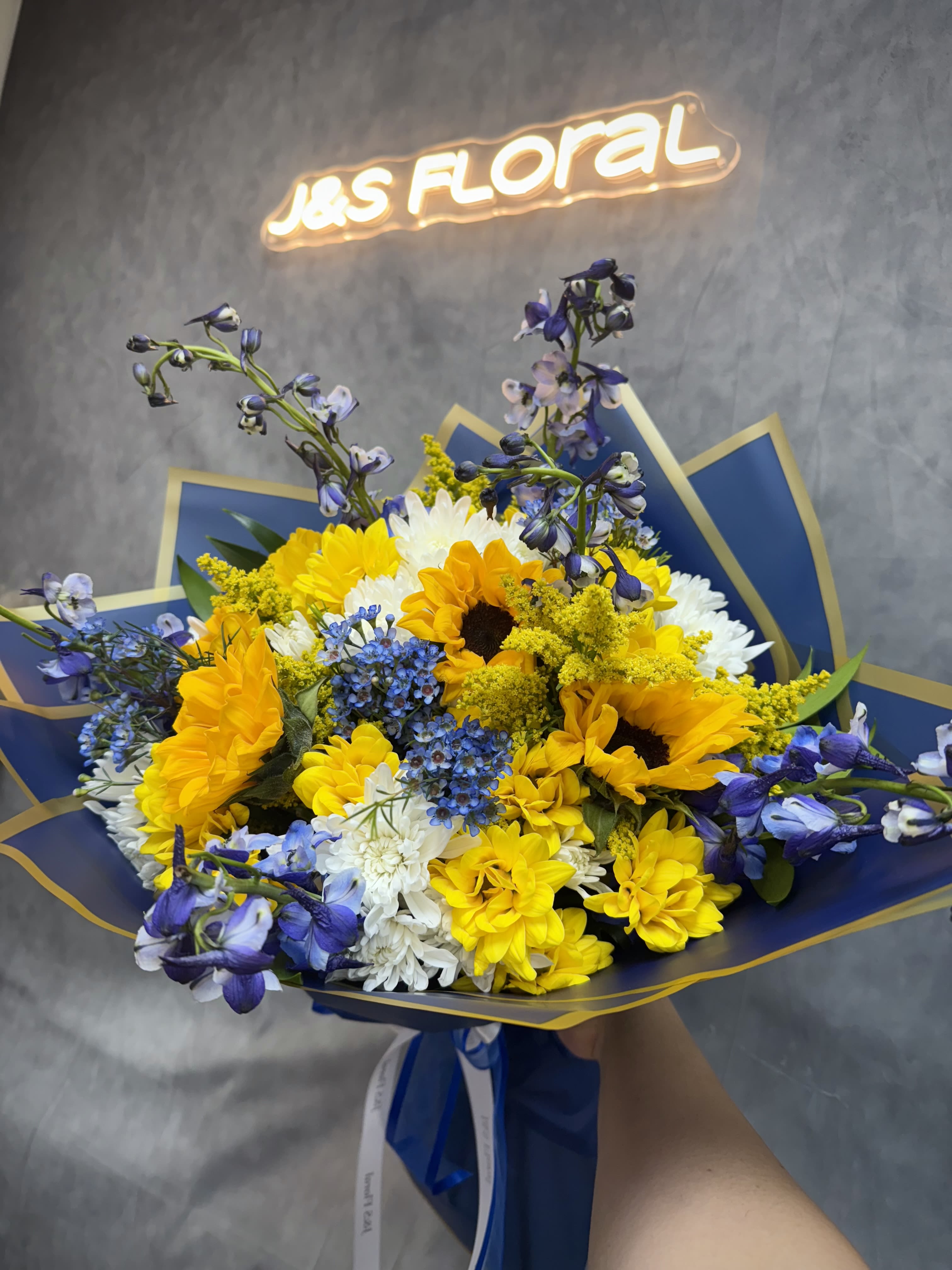The Starry Night Bouquet  - Inspired by Van Gogh, this stunning arrangement features sunflowers, daisies, delphiniums, and waxflowers in a vibrant palette of blues, yellows, and whites. Perfect for adding artistic flair to any occasion, this bouquet celebrates creativity and beauty in every bloom.