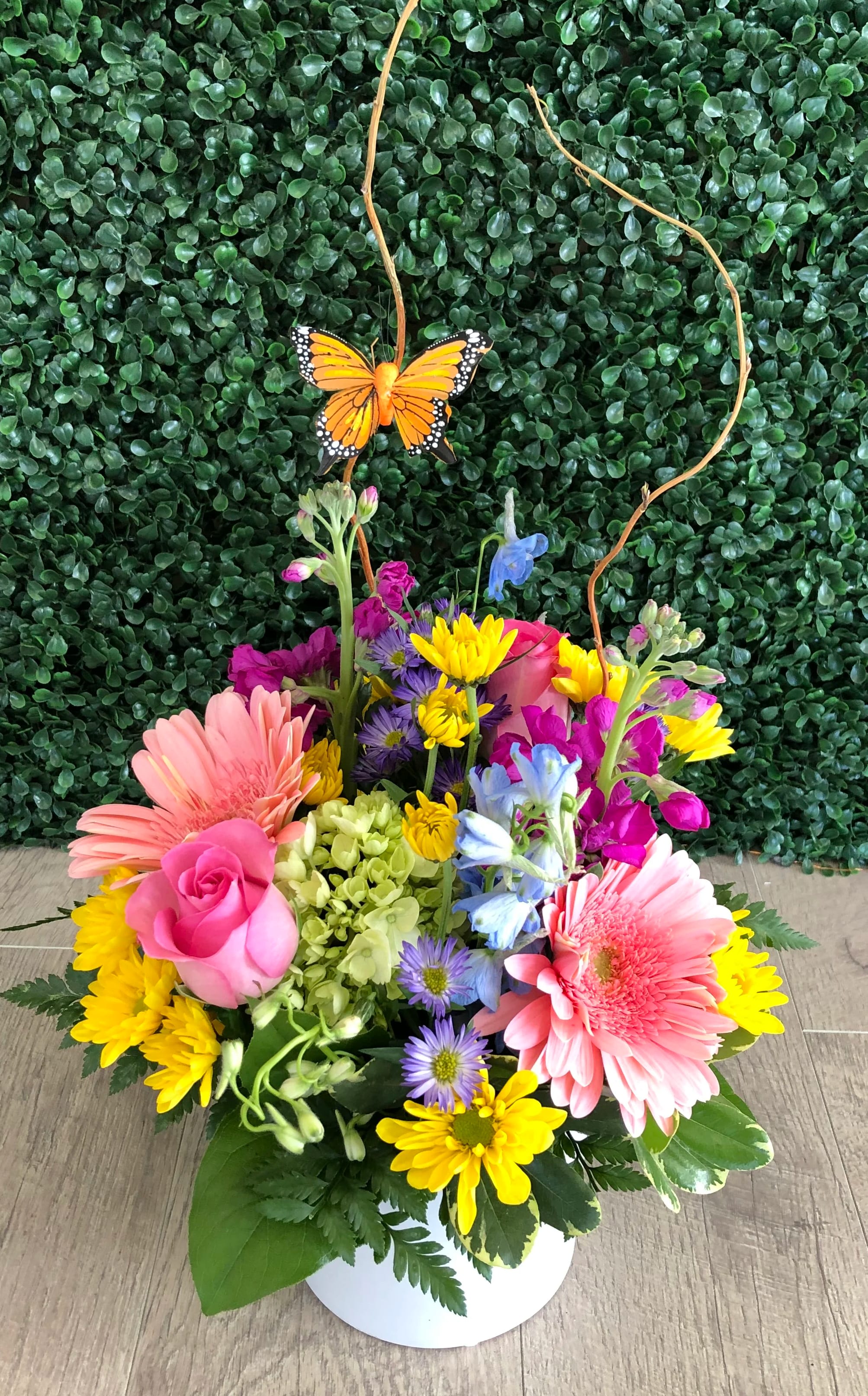 Spring Blooms Bouquet - Spring Blooms is filled with colorful flowers and love. Pink gerbera daisies, mini green hydrangea, pink roses, yellow daisies in a white cylinder vase Approx size 12" tall by 8" wide