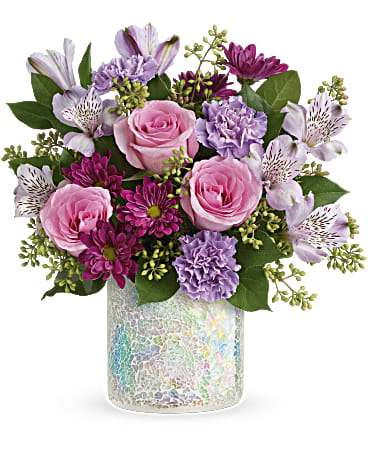 Shine In Style Bouquet - A cheerful mix of soft pink roses, lavender blooms, and vibrant purple accents is artfully arranged with fresh seasonal greenery in a shimmering keepsake glass vase. Playful yet elegant, Shine in Style brings a pop of color and a touch of sparkle to any space—perfect for birthdays, congratulations, celebrations, or simply brightening someone’s day.