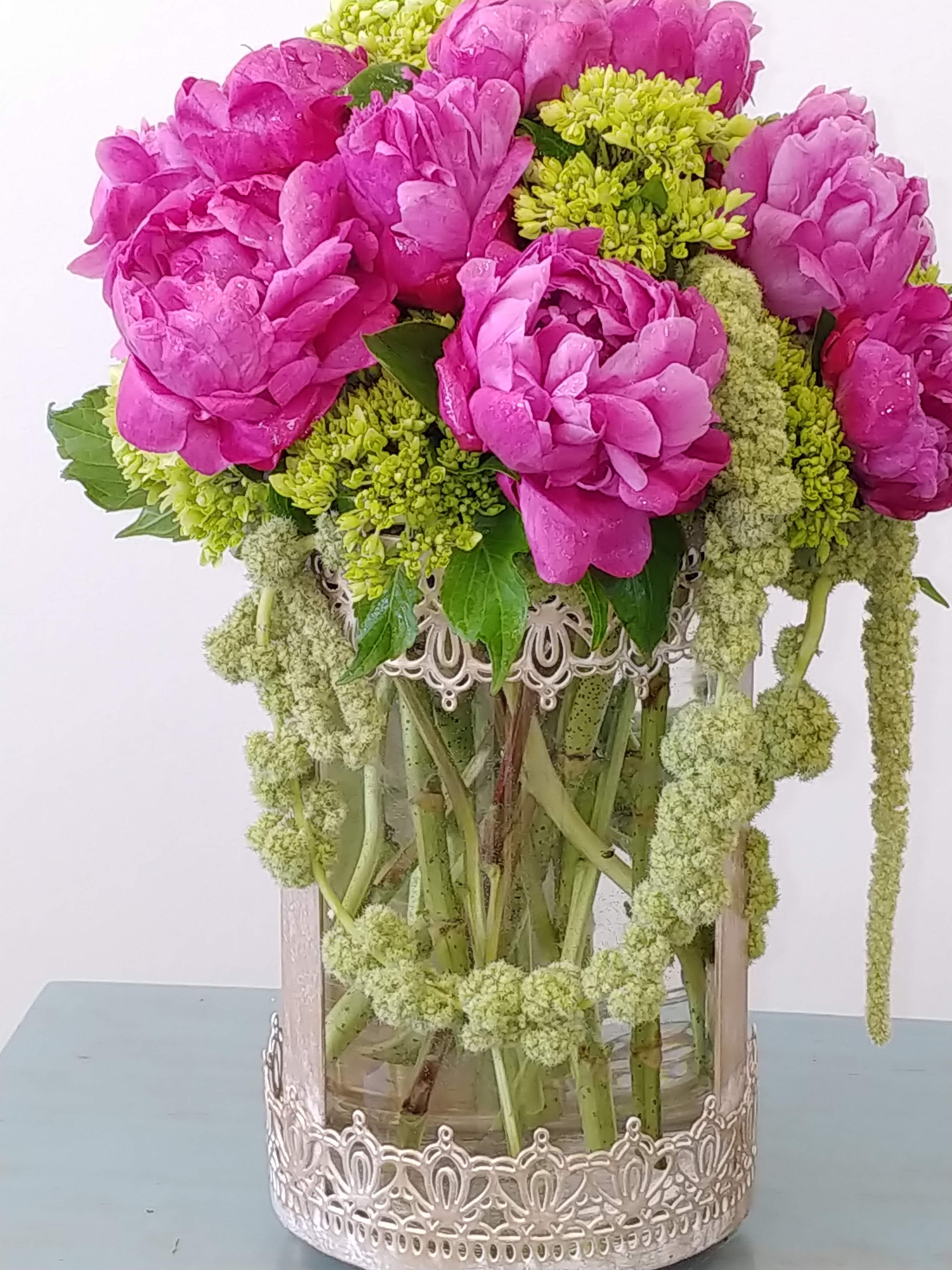 Luxury Blooms - Send luxury and decadence with this gorgeous floral arrangement.Pink and vibrant green textured floral. We use Peonies or lush big garden roses.We can guarantee we will  pick the freshest choice. The container in the photo is discontinued and we will replace with a comparable classy gold tall ribbed cylinder. 