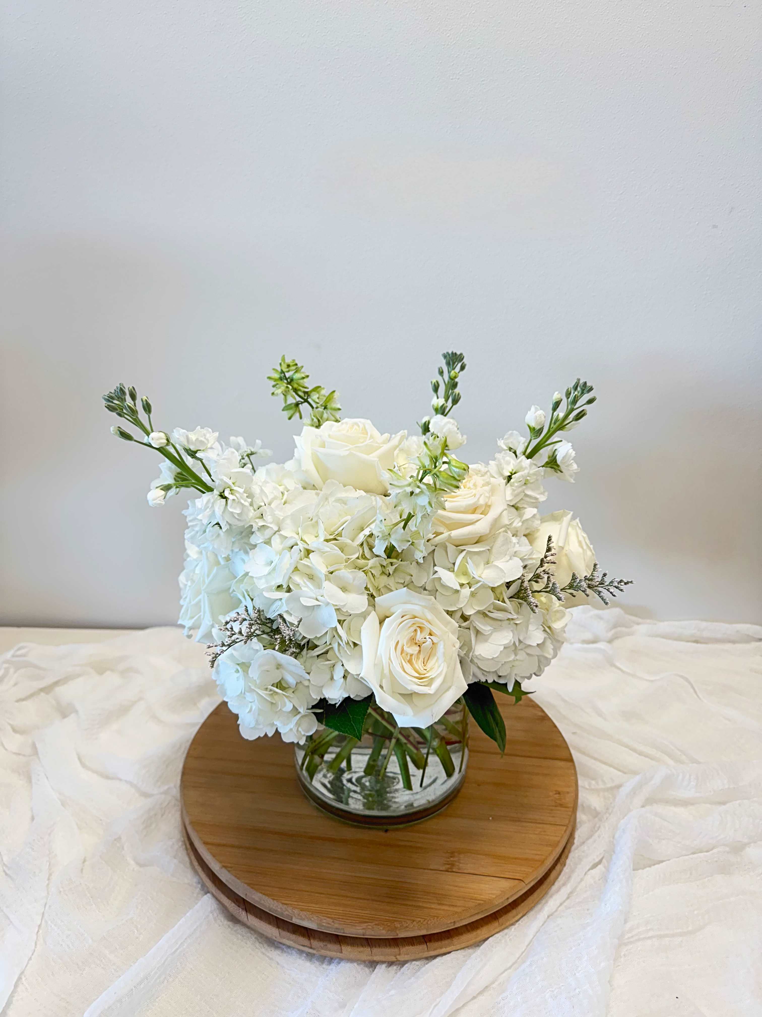 Purity  - This arrangement, designed in a clear glass vase, is neat and compact with crisp white blooms.  The blooms used may vary by the season and availability, and since each arrangement is custom-made to order by our talented designers, they will all look slightly different, which is what makes them so special!  The photo is a representation of the overall vibe of this Botanique signature arrangement. 