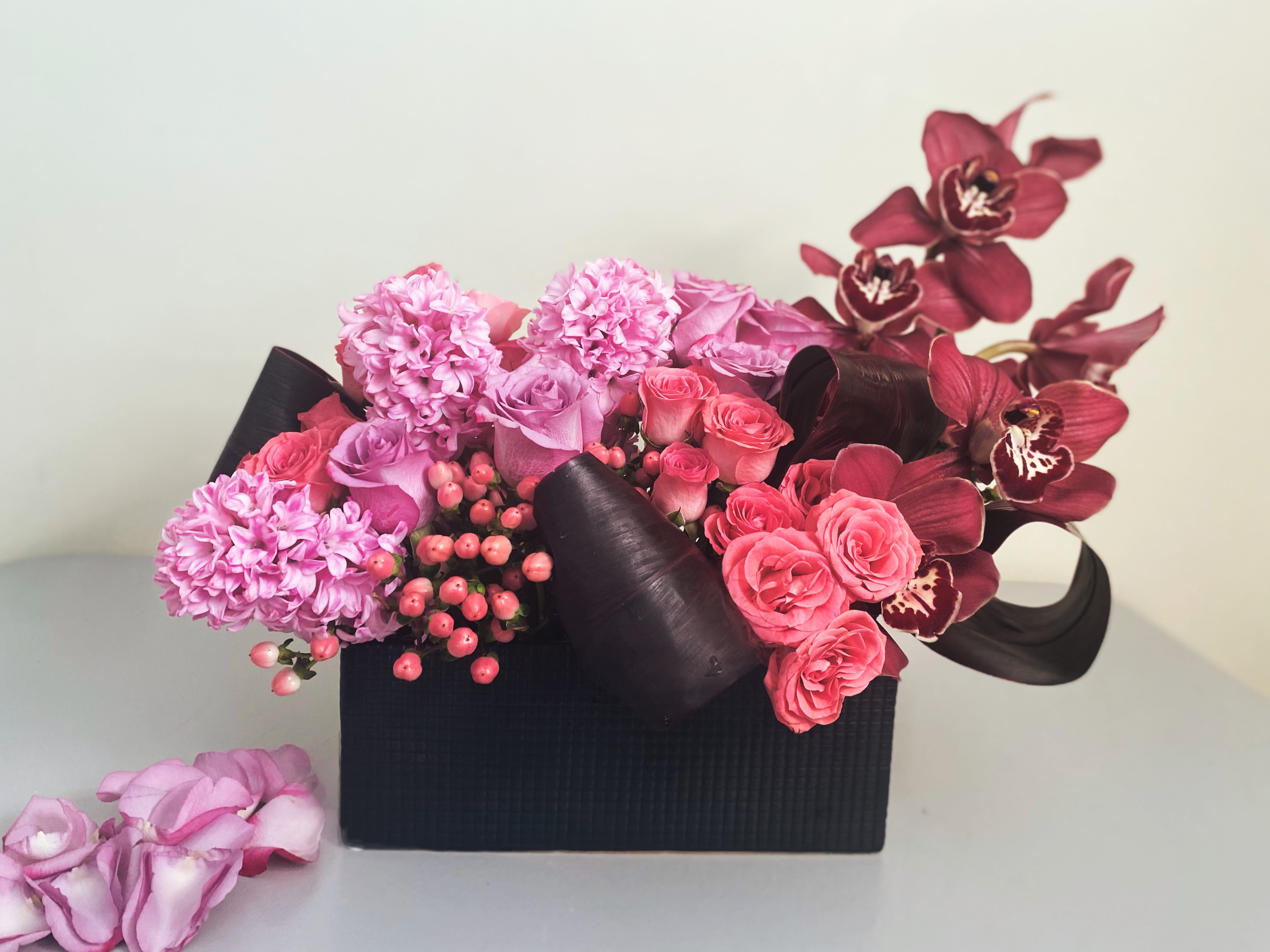 Pink And Black (attn: black vase on back order) - Modern lush design of pinks corals, lavender and burgundy in a sleek black container. We use the freshest flowers in the color palette and we may add or substitute for value and quality. Aprox 18x12 black vase is on back order, we are substituting with a white rectangle.