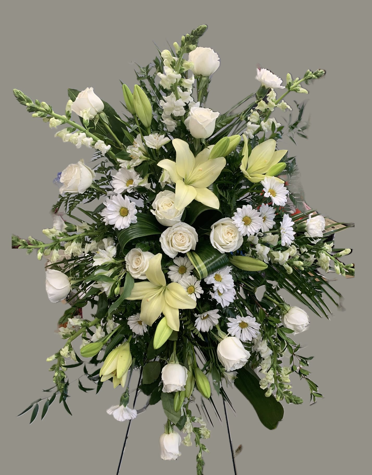 All White Standing Spray  - A breathtaking tribute to the one passed on. Displayed on a standing easel this piece is arranged with all white flowers of various types. Roses are the main focus tucked in among tea leaves, carnations, snapdragons, mini carnations and lilies. A wonderful way to show your care during a difficult time