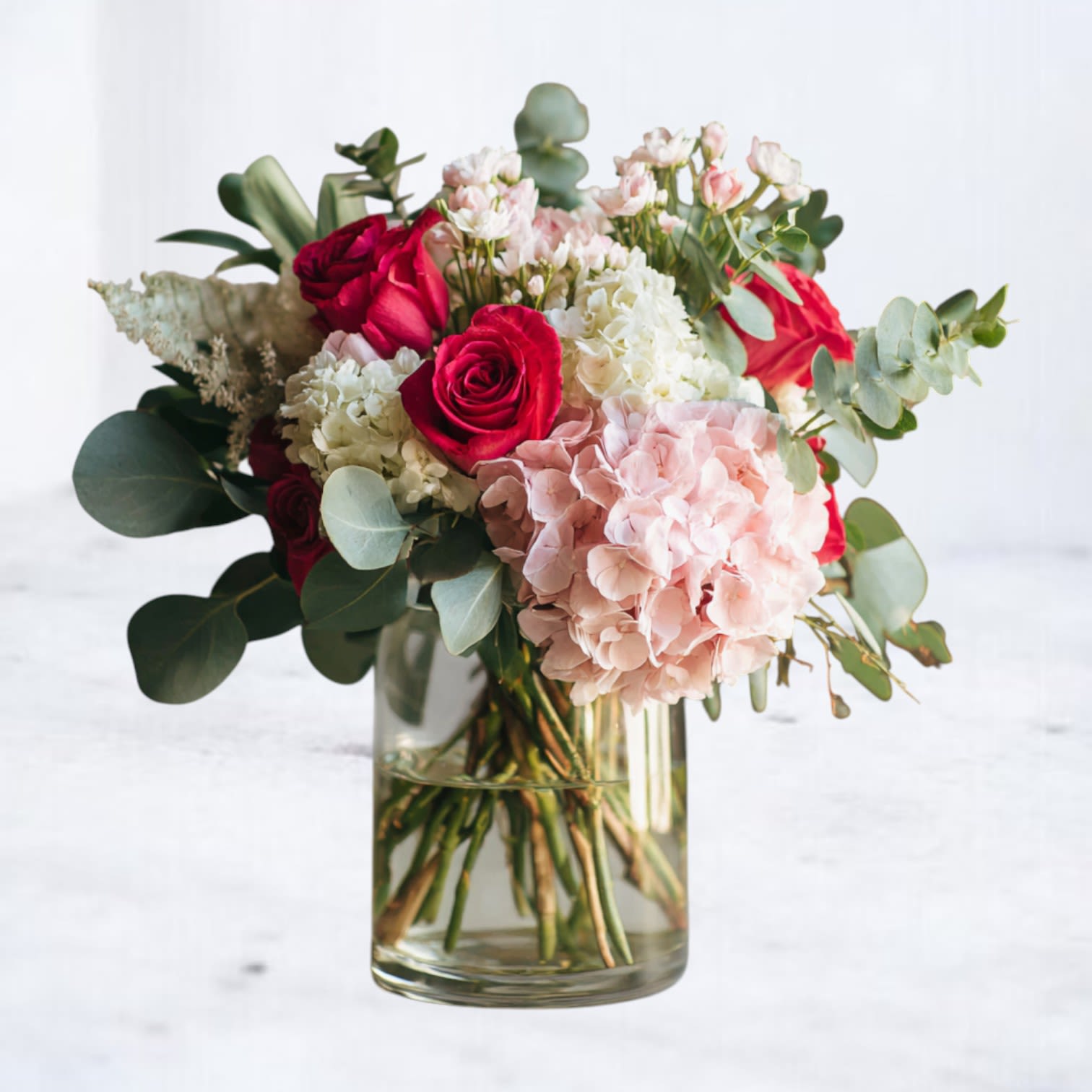 Velour Poise - Velour Poise is a refined Valentine’s arrangement designed to feel intimate, elegant, and intentional. A soft foundation of blush hydrangea is paired with premium red roses and balanced with airy seasonal accents, all arranged in a clear glass cylinder.  Rich in texture yet restrained in form, this bouquet offers a modern expression of Valentine’s flowers—thoughtful, polished, and quietly striking.