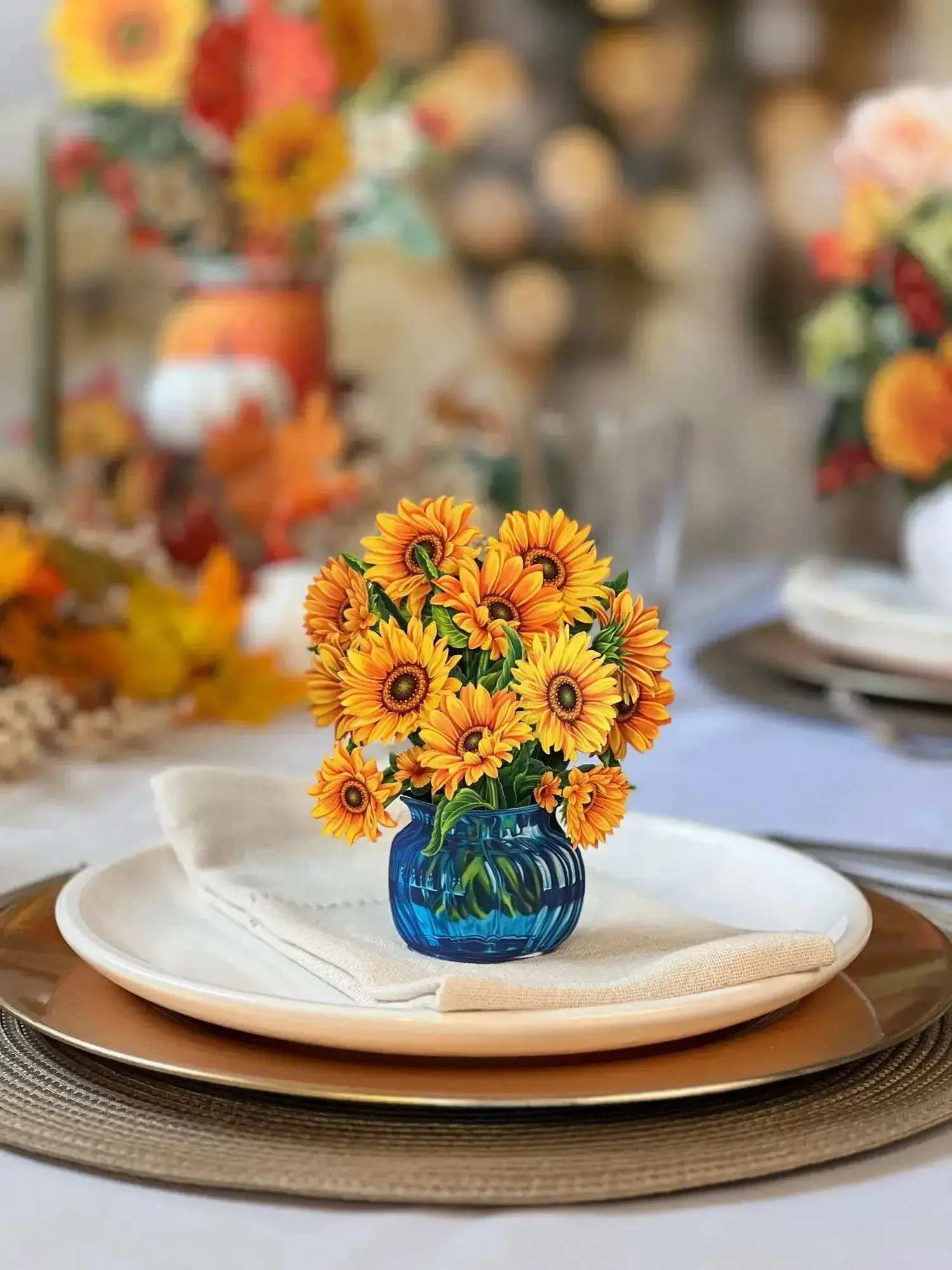 Mini Sunflowers Pop-Up Card - Bright, bold, and mini: FreshCut Paper’s Van Gogh inspired, unwilting sunflowers cheer every room, teaming with positivity and joy. The bodacious bouquet features an elevated design of bursting sunflowers in an understated and elegant blue, glass vase. Sunflowers represent adoration, loyalty, and longevity, making this adorable arrangement the perfect pick-me-up during life’s stormy weather, or a joyful reminder for those already shining.  Measures 5.5” high by 5” across