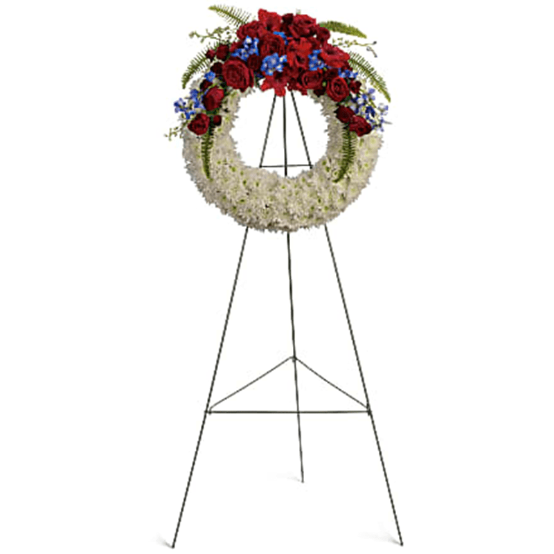 Reflections of Glory Wreath Standing Spray - An elegant ring of serene white flowers topped with bold red and blue blooms is a strong and loving tribute toa life distinguished by patriotism, honor and dedication to country. A distinctive sympathy wreath of traditional flowers such as red roses and gladioli, bright white chrysanthemums, and proud blue hydrangea and delphinium. Orientation: One-Sided