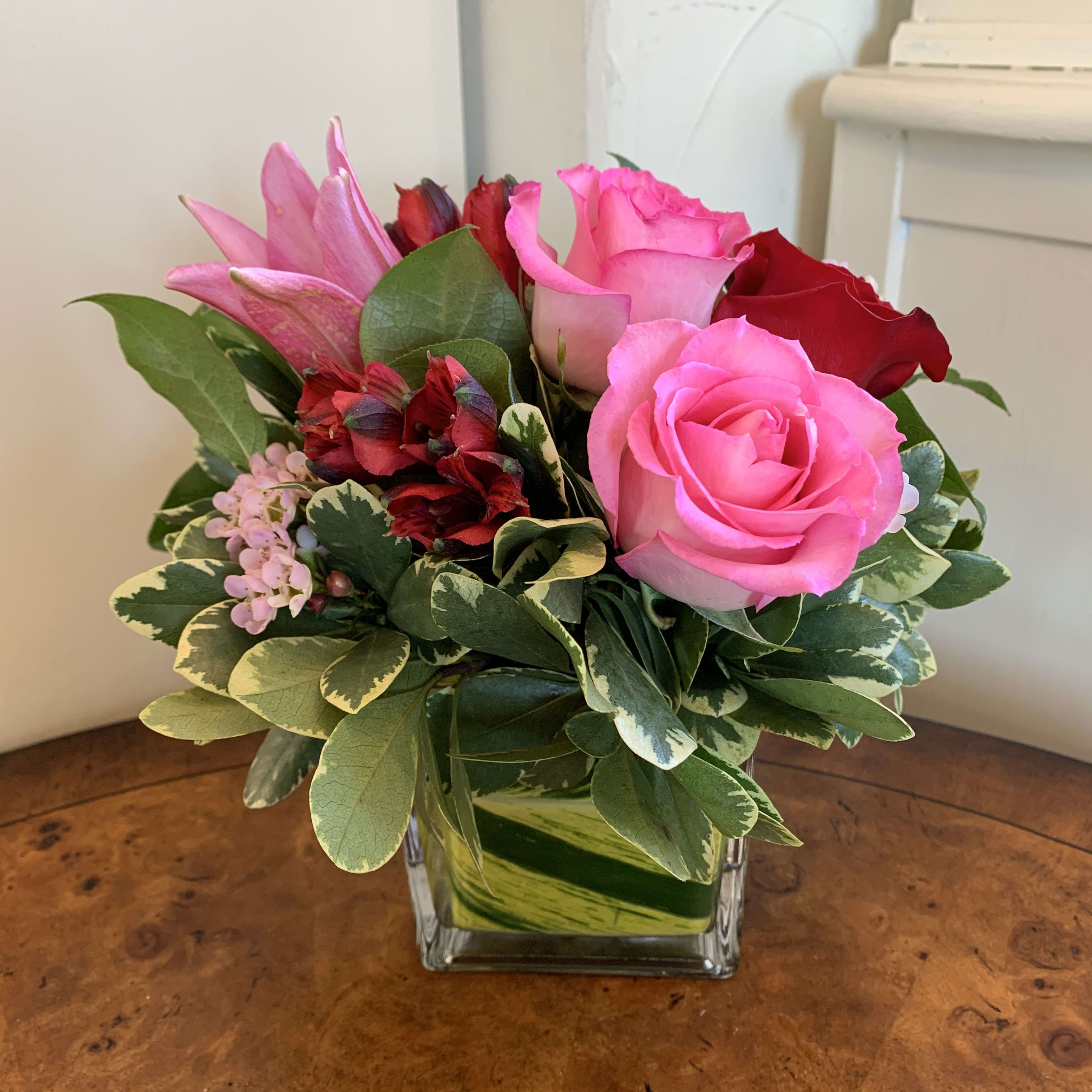 Happy Hearts Day  - Red and pink roses, pink lily, red alstromeria, arranged with pink waxflower in a leaf lined 4" cube vase. Approximatly 8" tall by 8" wide. 