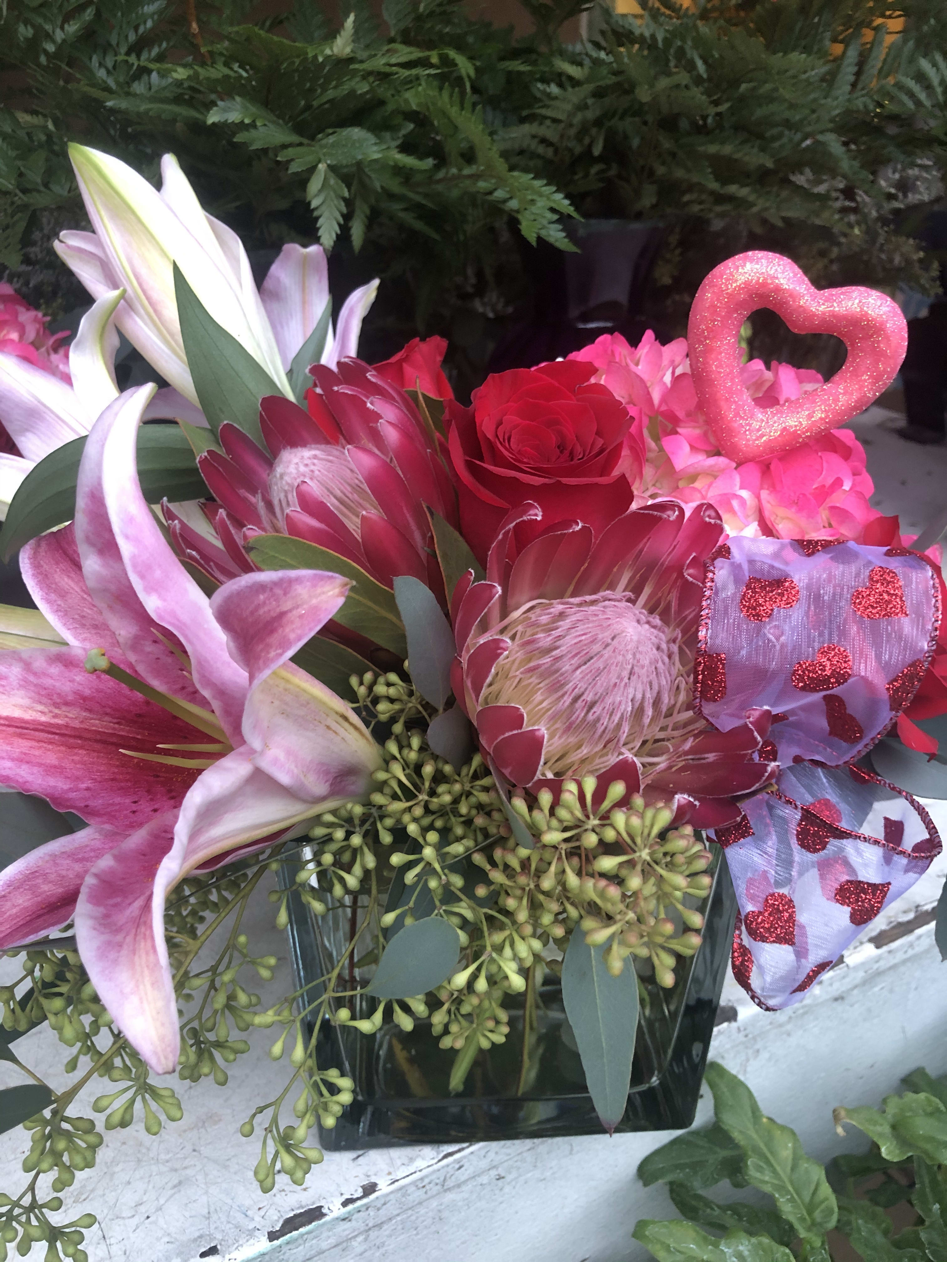 Signature valentines bouquet  - Pink hydrangea, roses, pink protea And oriental Lily’s in a cube vase with touches of seeded and silver dollar eucalyptus and a Valentine’s ribbon.  