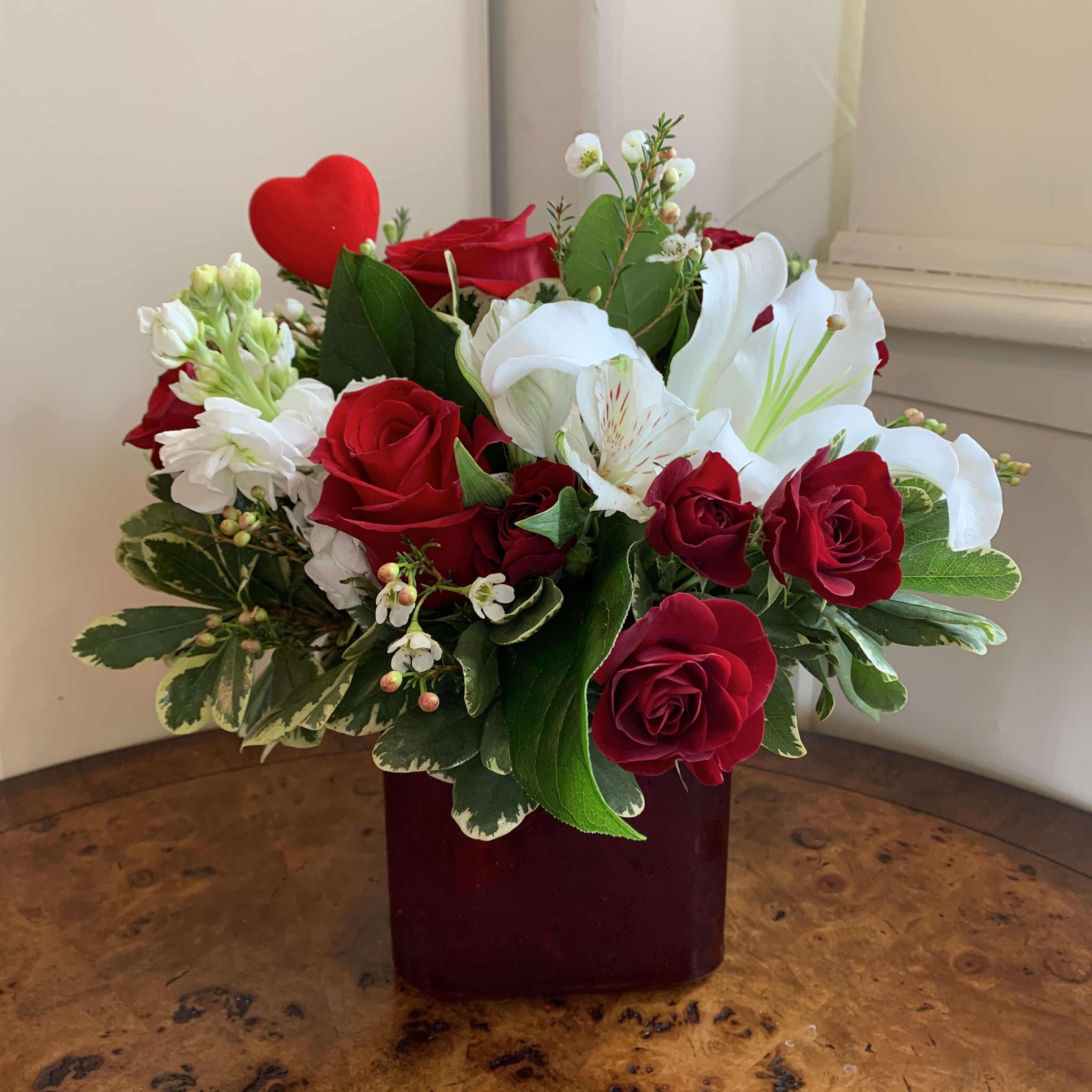 Garden Jewel - Red roses, white Casablanca lilies, white fragrant stock and alstromeria and filler flowers in a red cube vase with a red mini heart