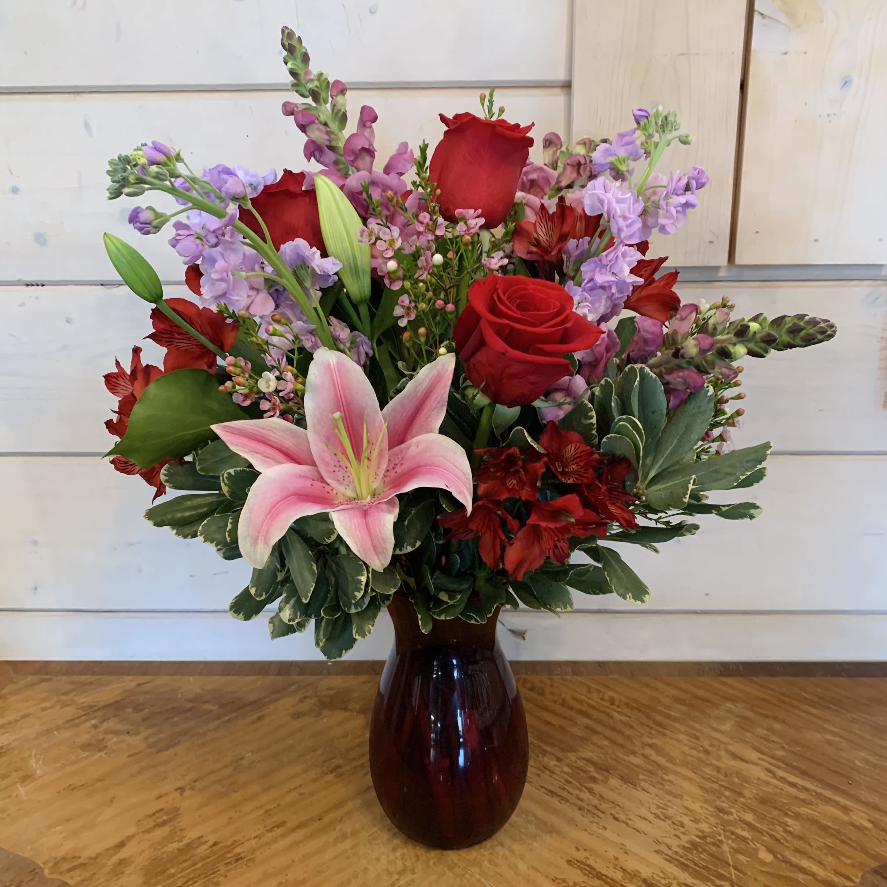 Higher Love Bouquet - Red roses and stargazer lilies with lavender snapdragons and lavender stock arranged in a 8" red Jordan vase with red alstroemeria and seasonal filler flower. Approximately 20" tall and 14" wide.  