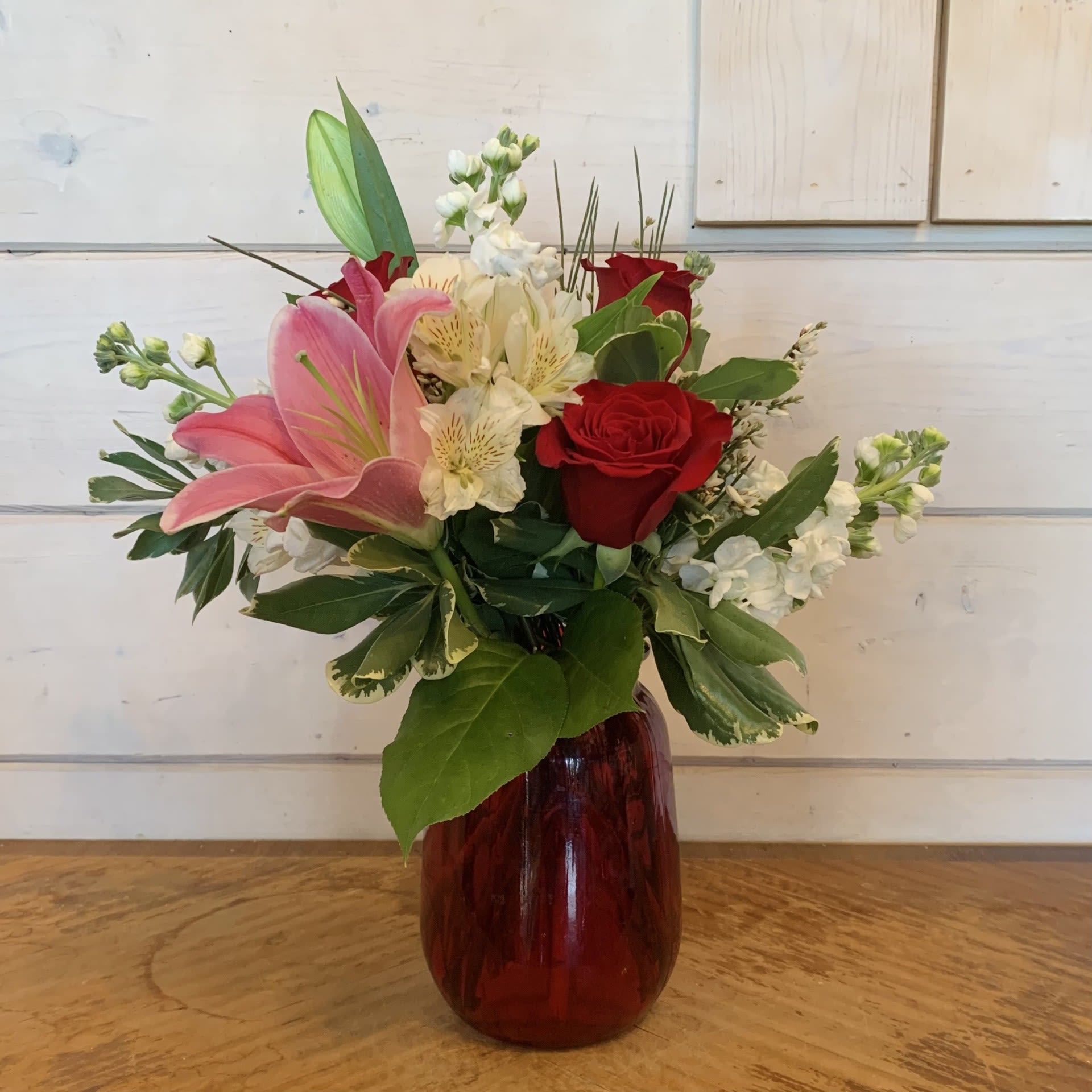 Hearts Wishes - Red roses, fragrant pink lilies and white stock, arranged in a red tulip vase with white alstroemeria and seasonal filler flower. Approximately 15" tall and 9" wide.