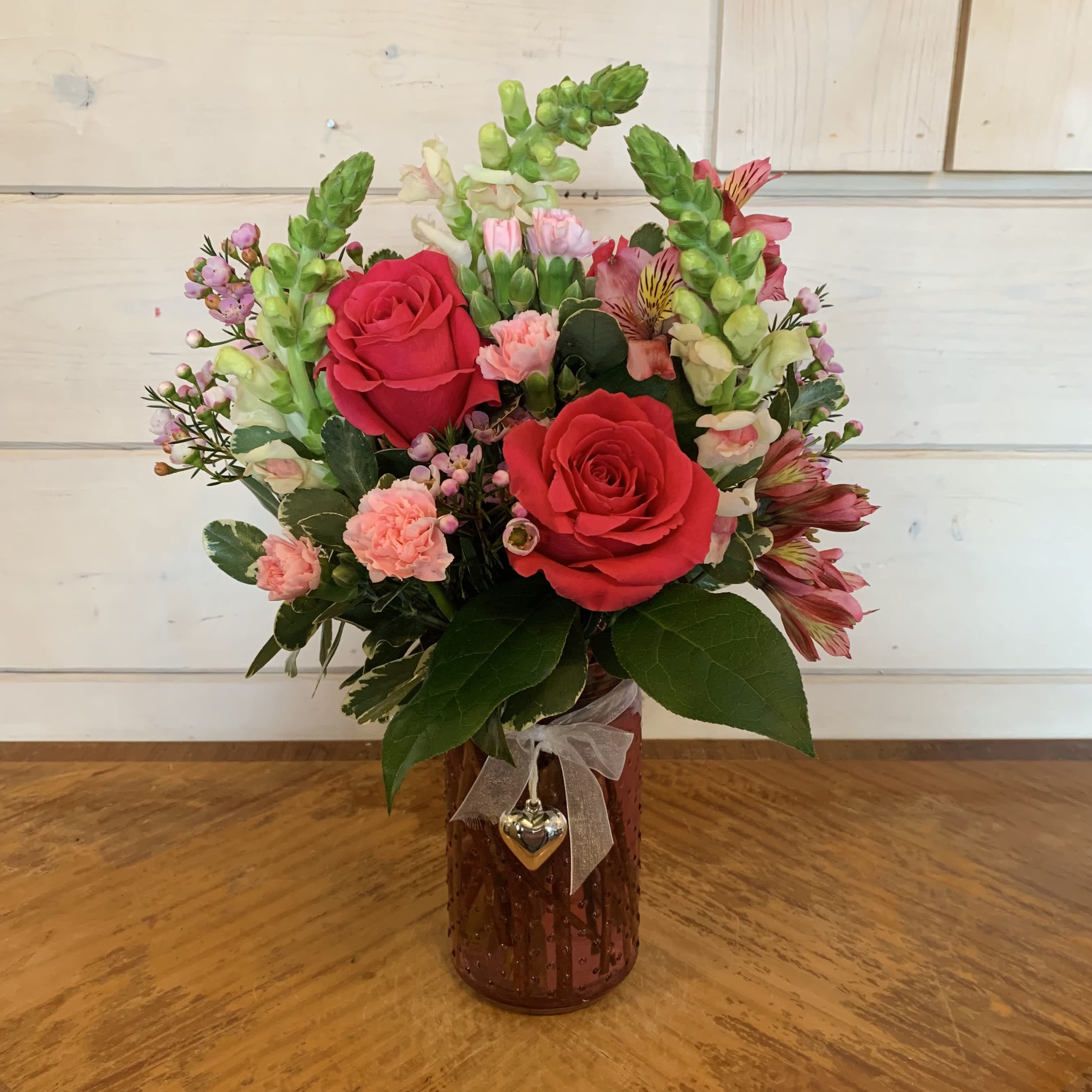 Hot Pink Posie - Hot pink roses, pink snapdragons, light pink mini carnations, hot pink alstroemeria and seasonal filler flower arranged in a 7" pink textured jar with heart pendant. Approximately 14" tall and 9" wide.