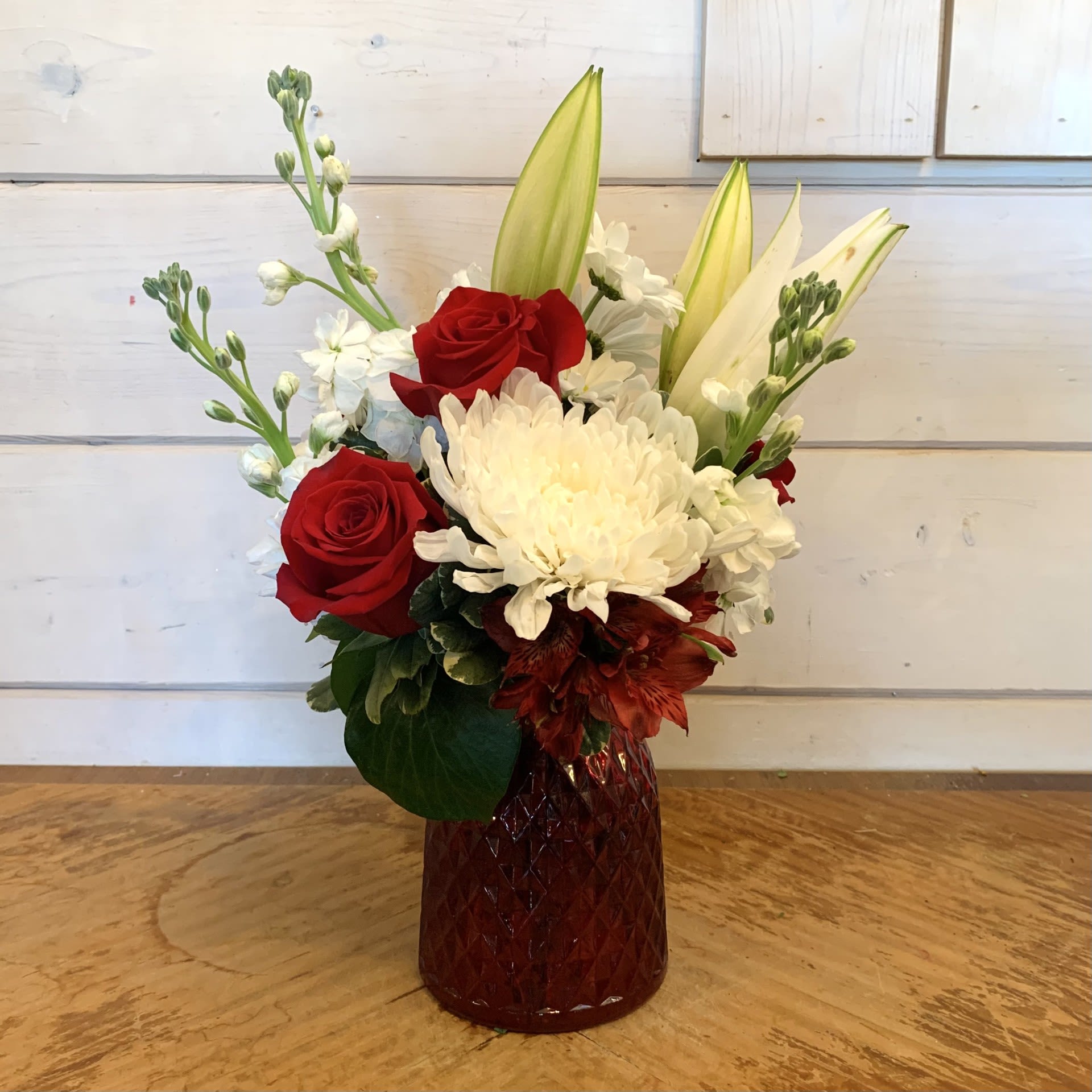 Mon Cheri Amor - Red roses and white lilies with fragrant white stock, white chrysanthemums and red alstroemeria in a red medium cut glass posy vase. Approximately 13" high by 9" wide. 