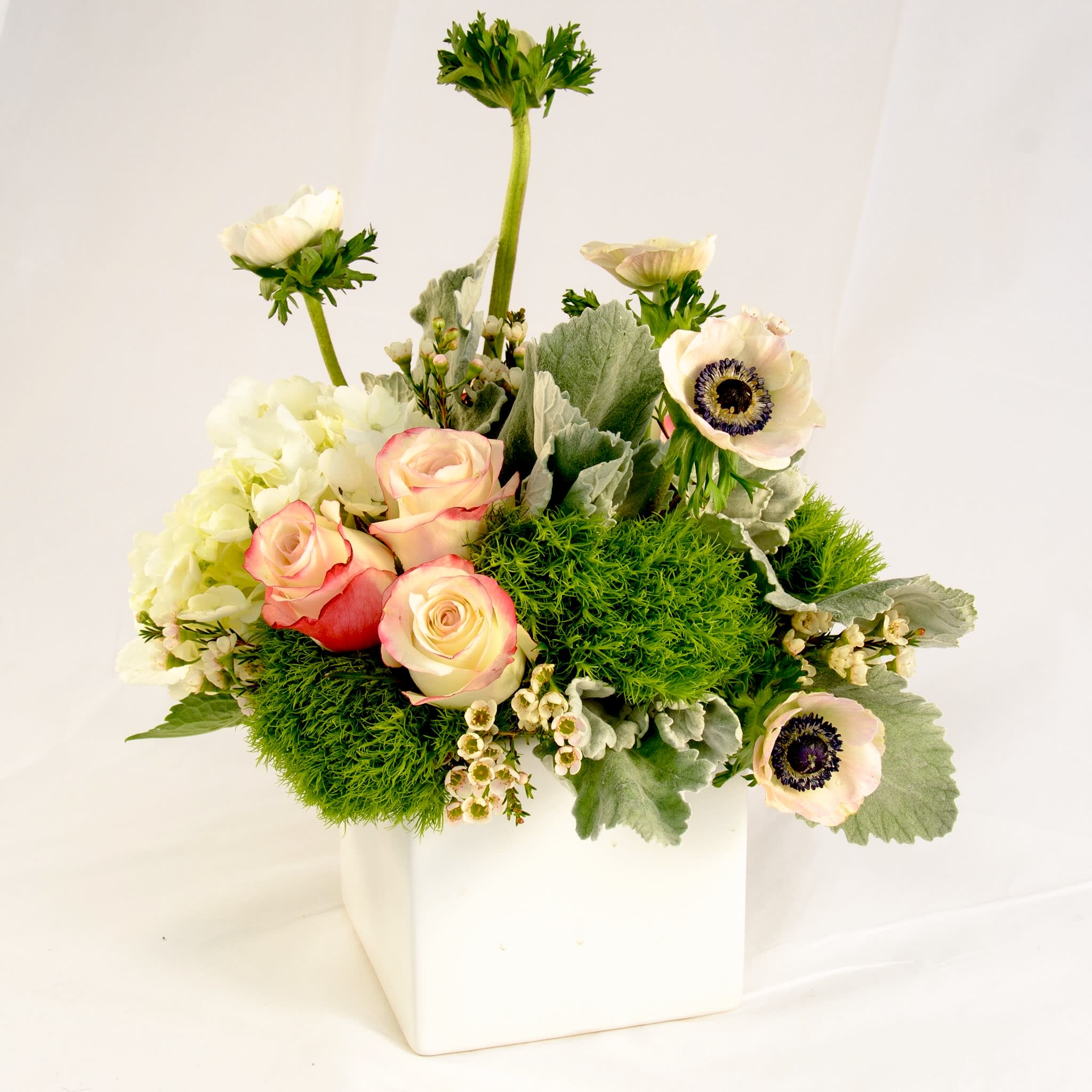 Brigitte - A gathering of unique flowers: peach roses, hydrangea, dianthus, dusty miller, wax flowers and anemone. Soft pastel palette mixed with natural green. Time to celebrate! (Approx. size 10"w x 12"h x 10"d)