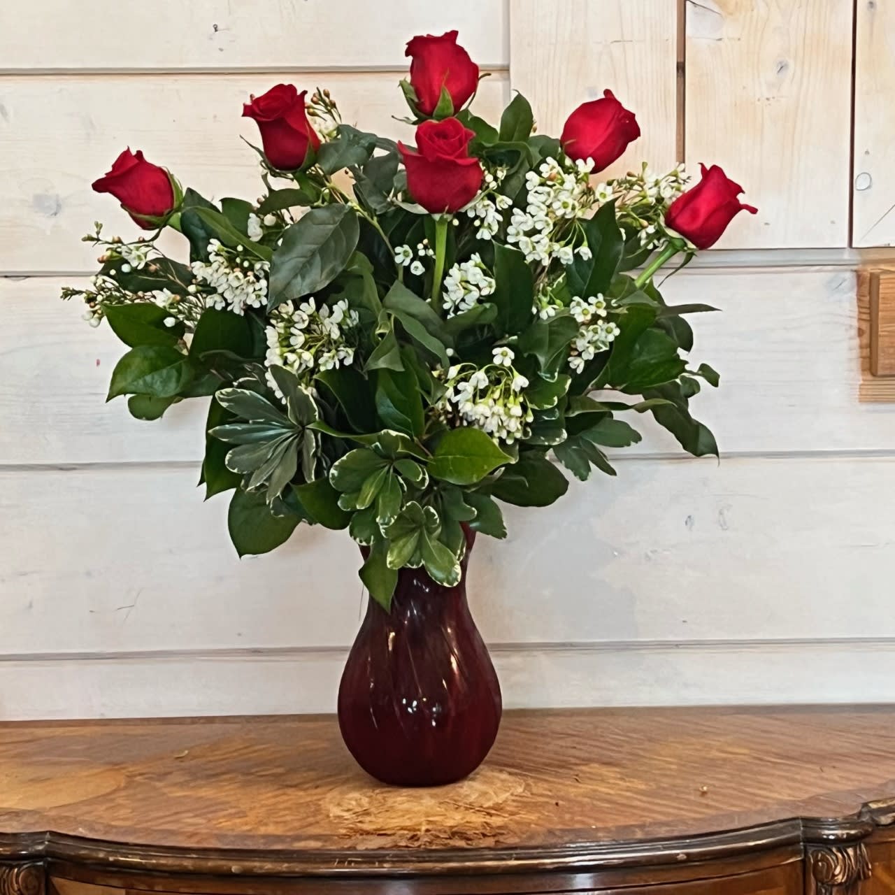 The Half Dozen Red Rose Bouquet - 6 premium long stem red roses arranged in a red swirl vase with premium greens and complimenting filler flowers. Approximately 22" tall and 16" Wide