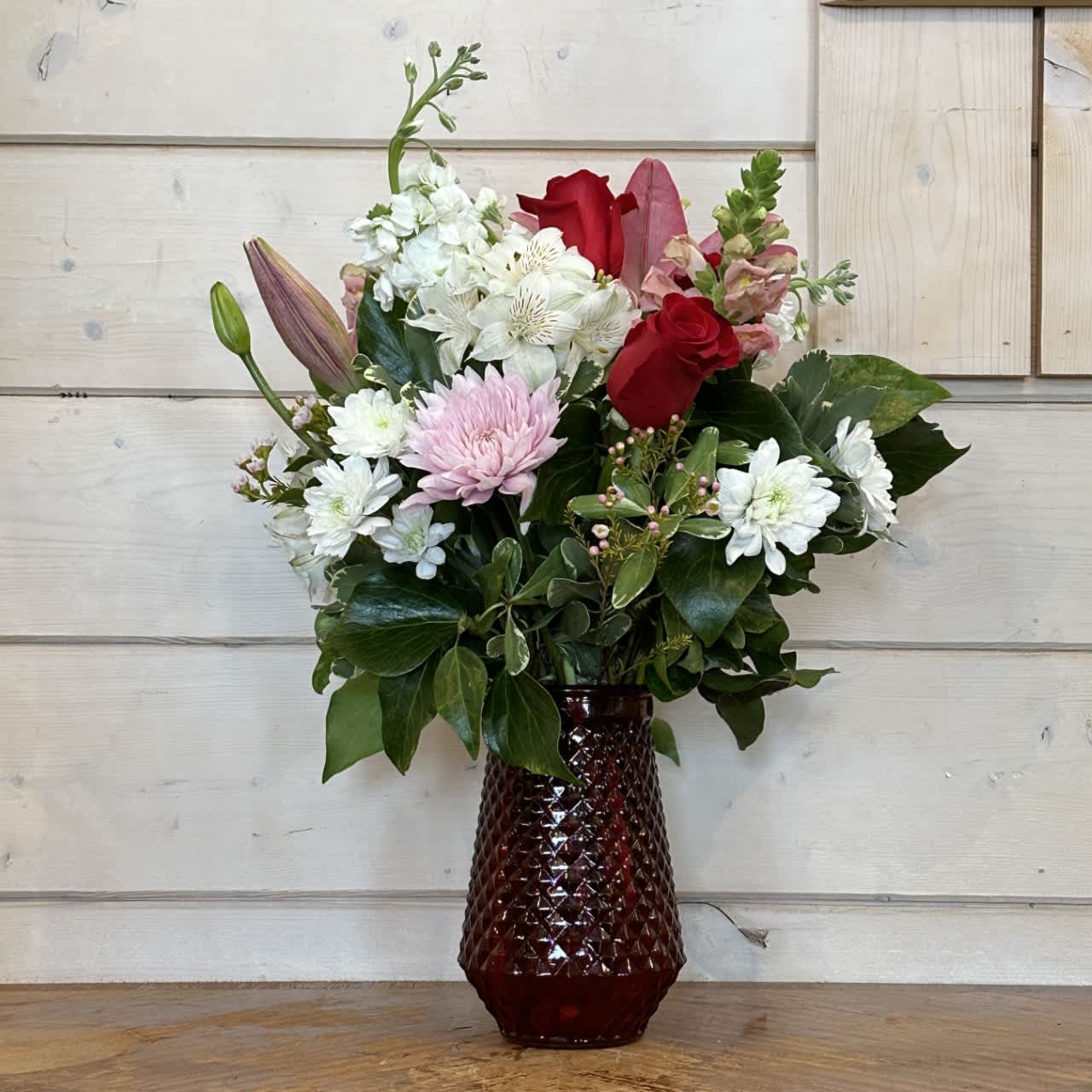 The Love Sonett Bouquet - Red roses, white stock, lavender snapdragons, burgundy lilies, white and pink chrysanthemums arranged in a tall red textured vase with seasonal filler flowers. Approximately 20in tall and 15in wide 