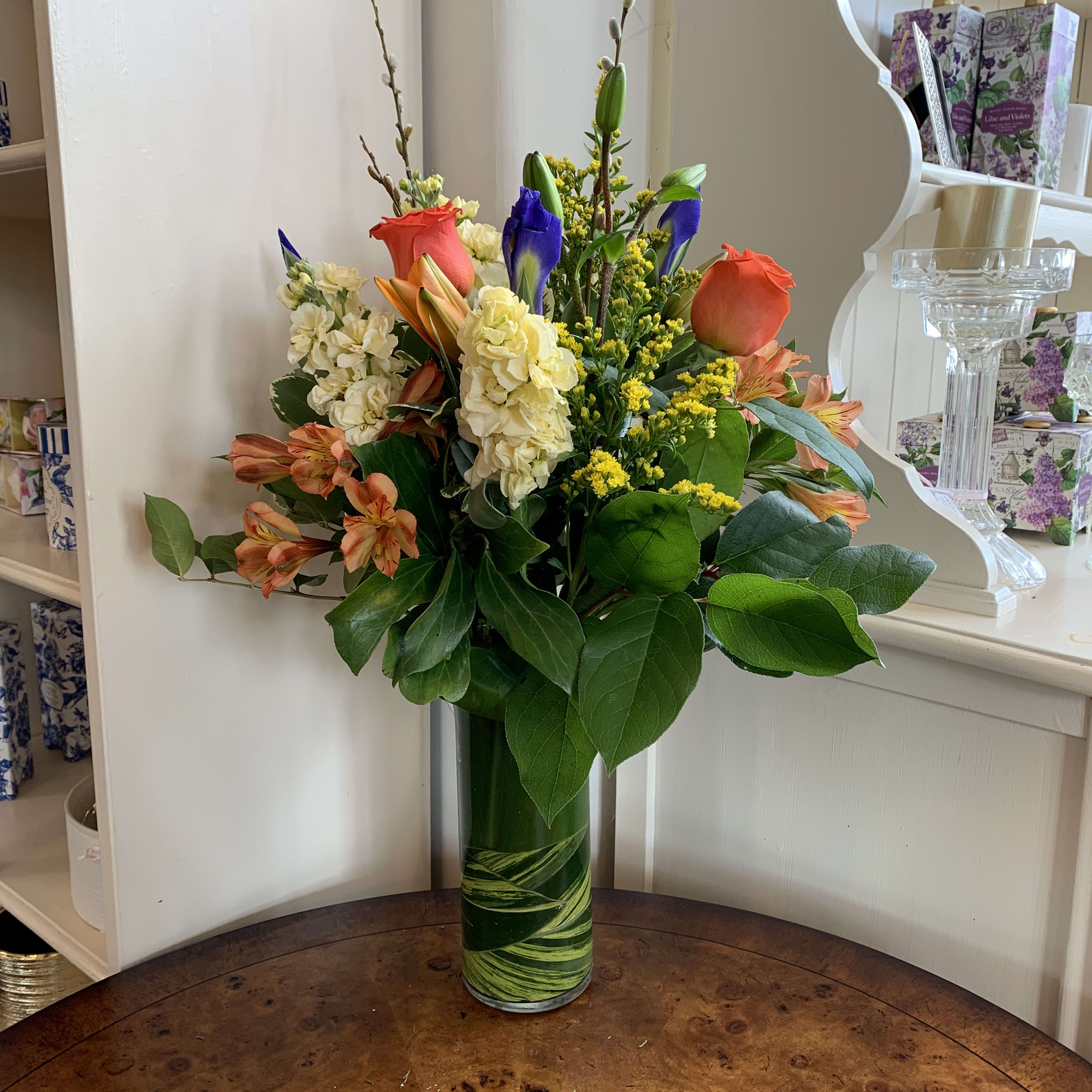 Joyful Greetings  - Orange roses, yellow stock, orange lilies, iris, orange alstromeria arranged in a leaf lined 9in cylinder vase with solidago and pussy willow branches. Approximately 18in tall and 12in wide.   