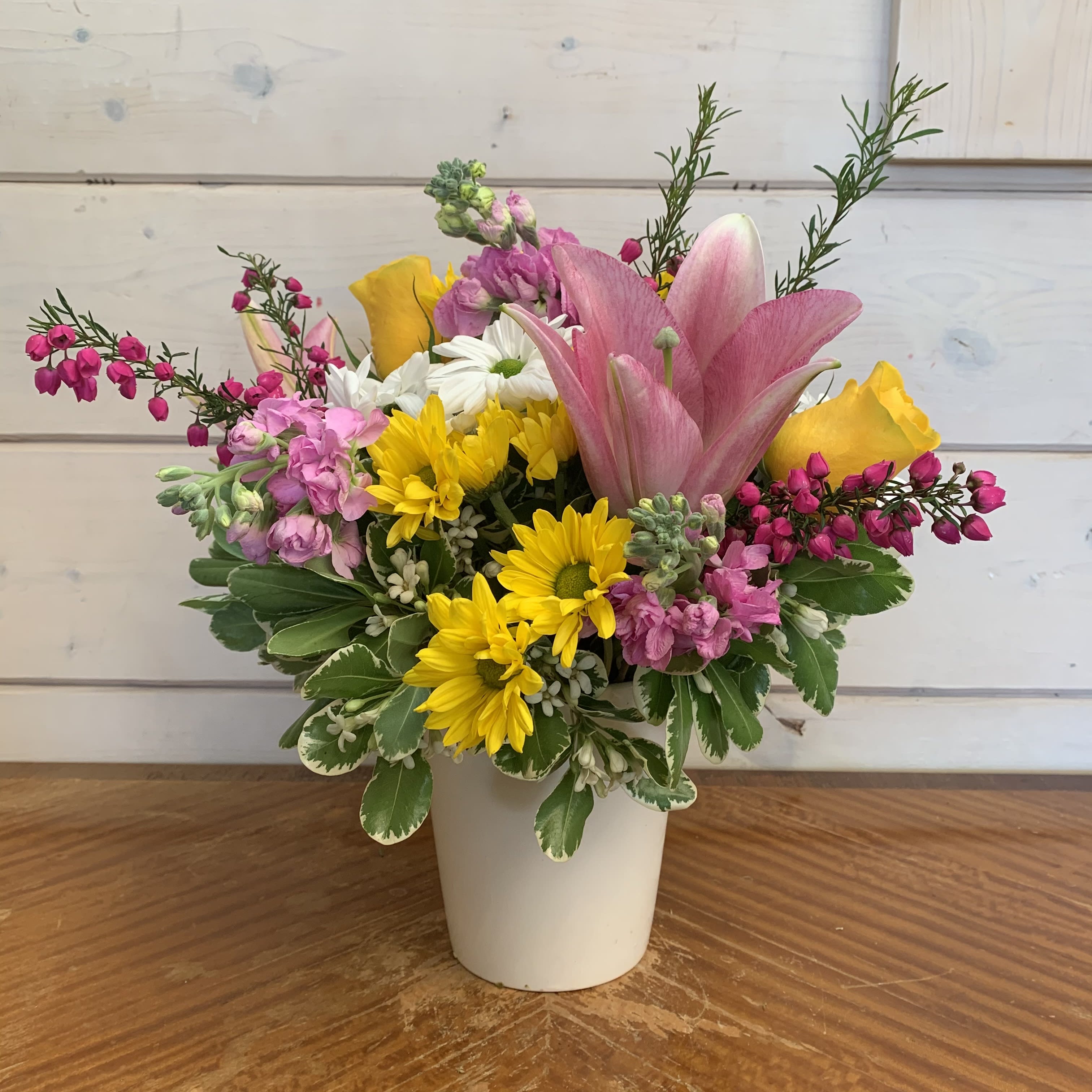 Darling Daisies  - Yellow roses, pink dancer lily, light pink stock, yellow and white daisies arranged in a white cache pot with seasonal hot pink beronia. Approximately 12in tall and 10in wide.  