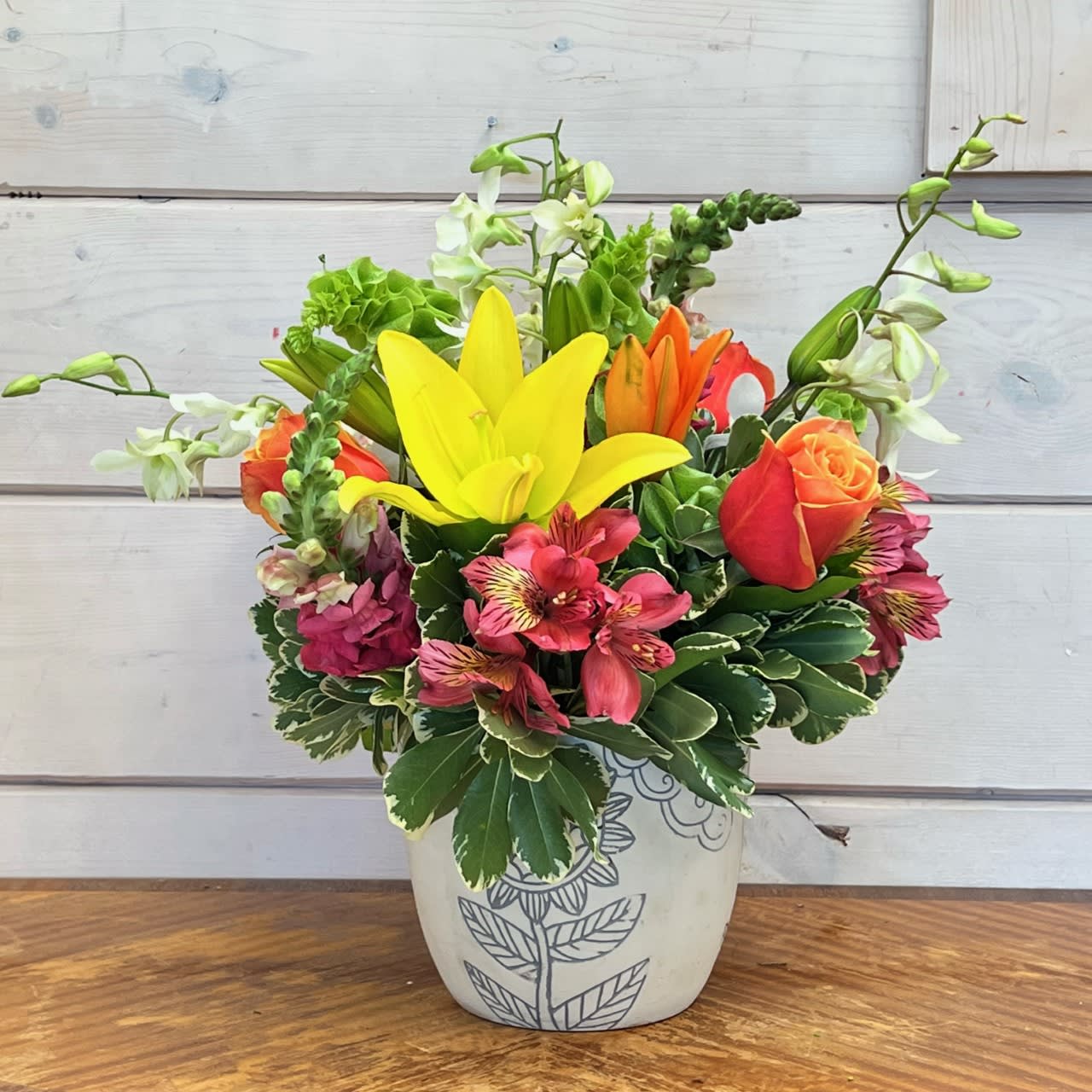 Tropical Summer Bouquet  - White orchids, orange roses, yellow and orange asiatic lilies, hot pink snapdragons, and bells of Ireland arranged in a cream color pot engraved with grey flower designs with hot pink alstroemeria and other seasonal filler flowers. 