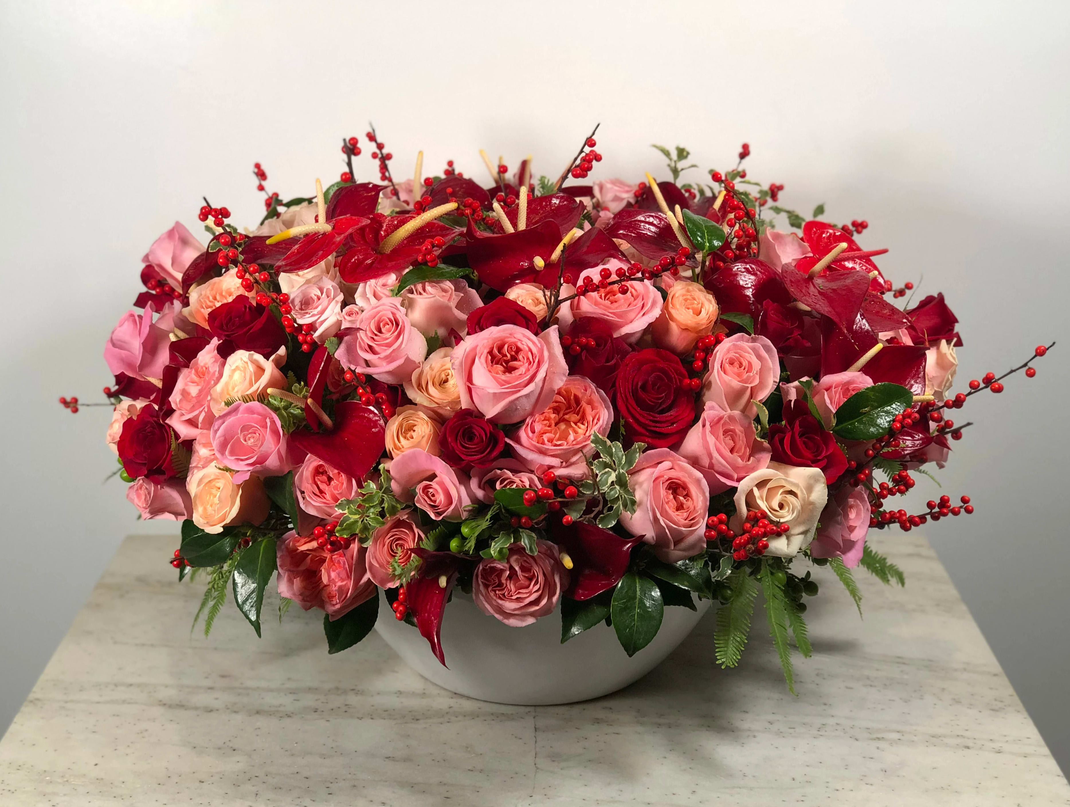 Red Porcelain - A bold medley of red, pink, and peach Roses with accents of luxurious red Anthurium makes this a truly stunning gift in a luxurious ceramic vase. The perfect gift for that special someone in your life!