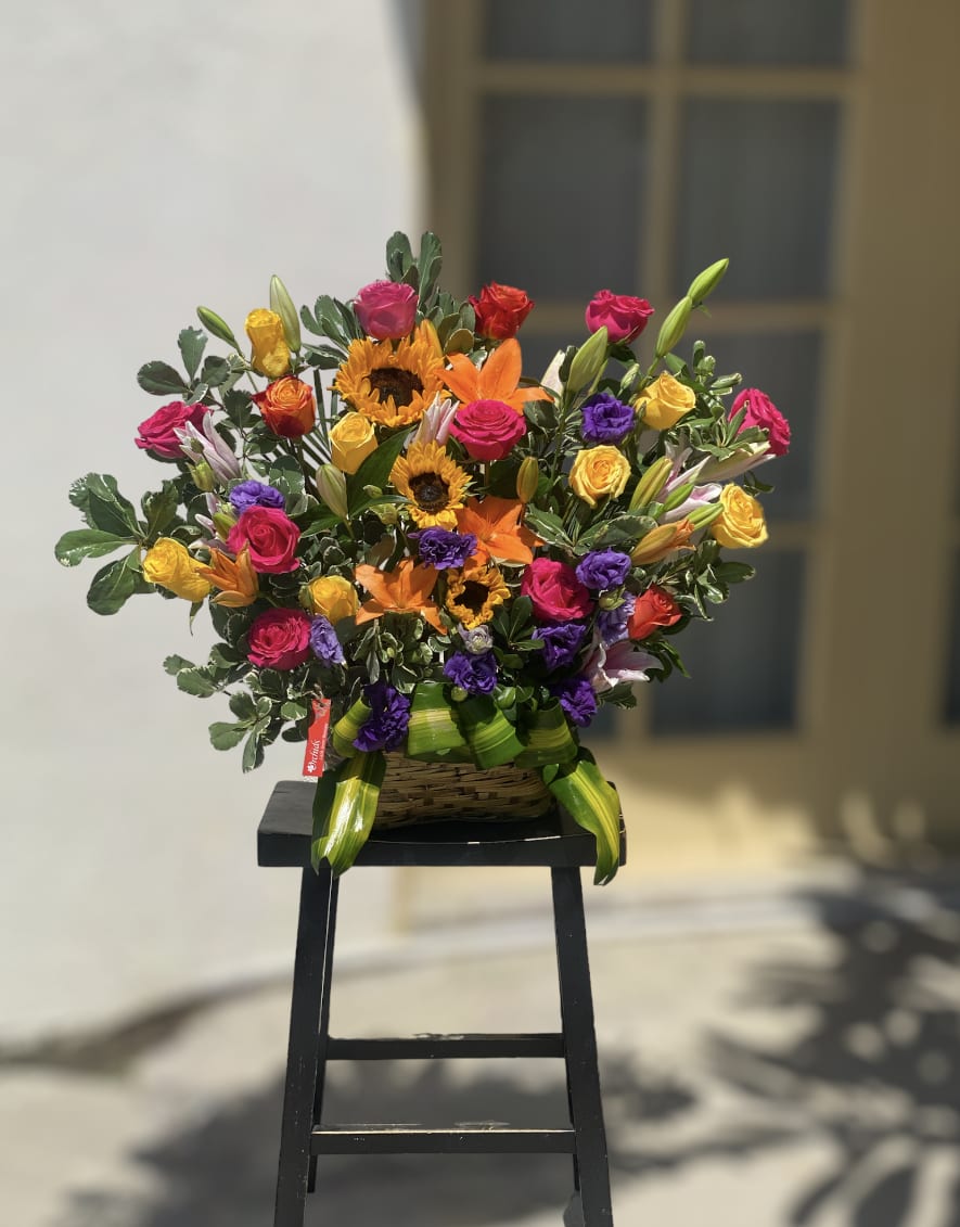 Sunflower Lisianthus Rose Garden Mix Basket - Send a gift of style and elegance with Orchids Little Secret Boutique  arrangement of sunflowers, purple lisianthus, orange roses, hot pink roses, yellow roses, accented with lilies, arranged in 6" H  basket. This bright color combination makes it the perfect get-well or birthday gift that will make their day!  Arrangement measures approximately 24"H 