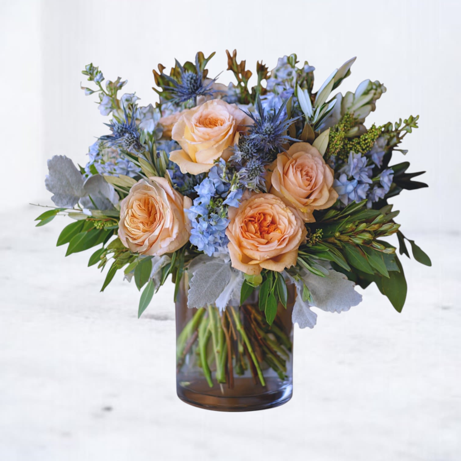 Morning Light Bouquet - The Morning Light Bouquet captures the serene beauty of a new day with its pastel blend of peach roses, creamy ivory blooms, and soft blue hydrangeas. Accented with delicate white stock and fresh eucalyptus, this arrangement is designed in a clear glass vase for a modern yet timeless look. Perfect for birthdays, anniversaries, welcoming a new baby, or simply brightening someone’s day, this bouquet radiates warmth and joy with every petal. Available for same-day flower delivery in Houston, Magnolia, The Woodlands, Spring, Conroe, and surrounding areas.