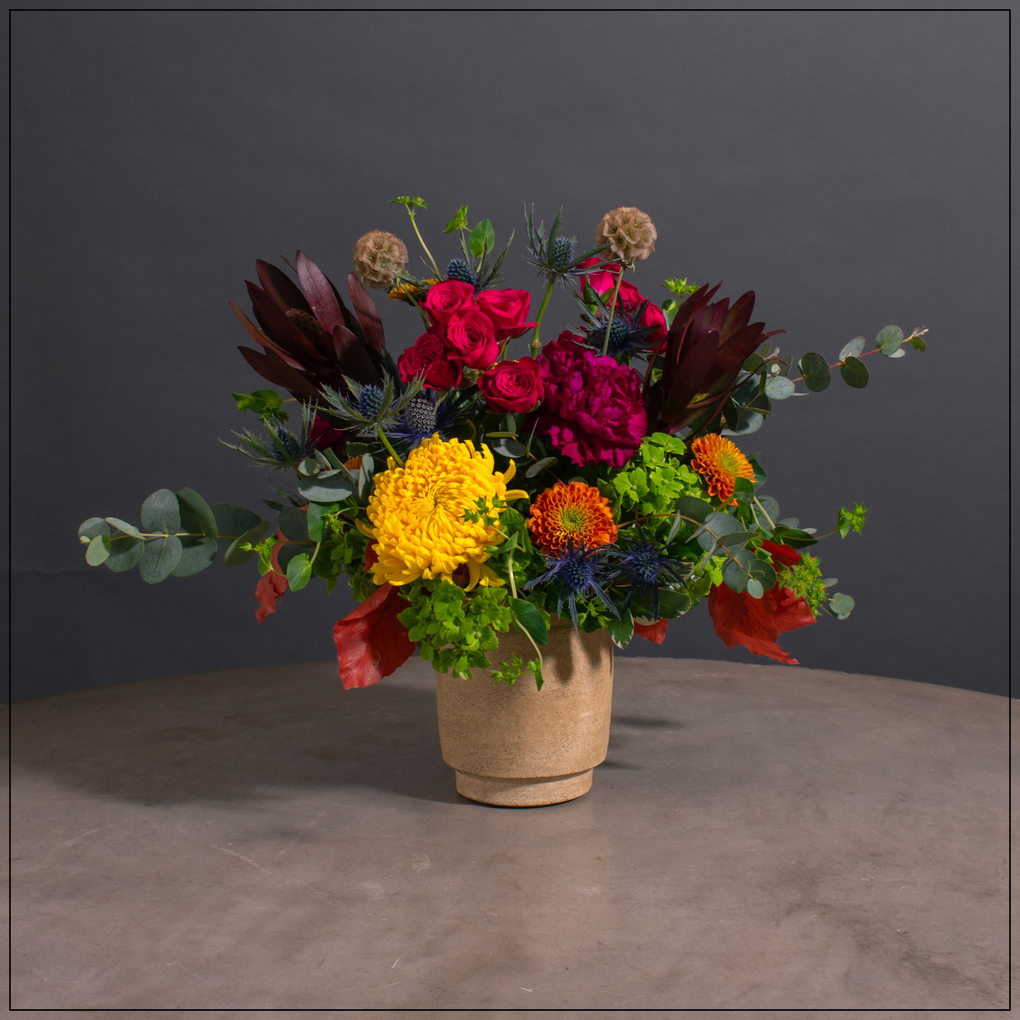 Olla - Sandstone colored pot with hydrangeas, protea, cremon, spray rose, daisy poms, eryngium, carnations, dried fall leaves and scabiosa pods,  Approximate size 13" w x 13" h