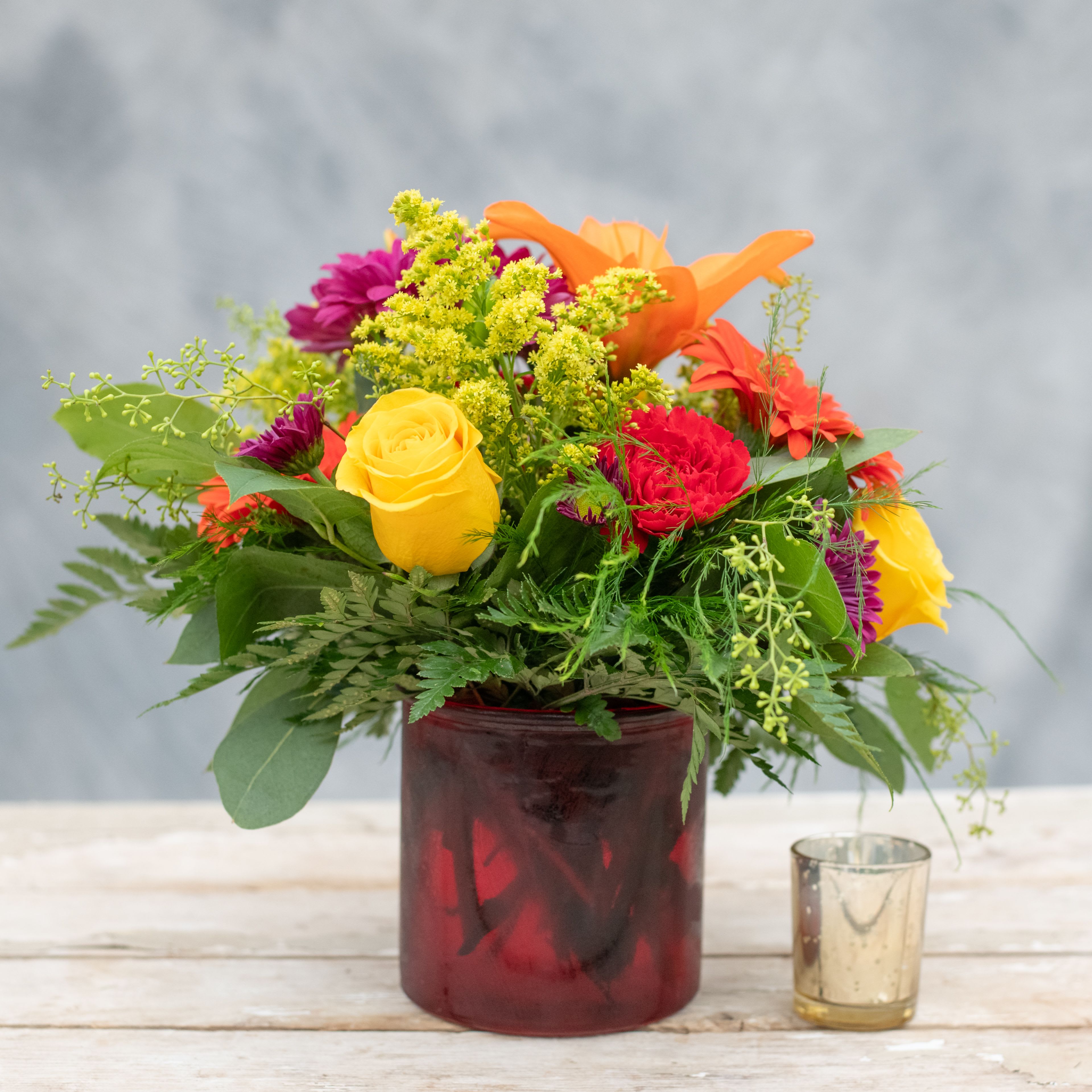 Starburst - Enjoy this explosion of color from a ruby red cylinder with yellow roses, orange gerbera daisies purple daisies, orange lilies and more.  A great arrangement for a coffee or side table.  