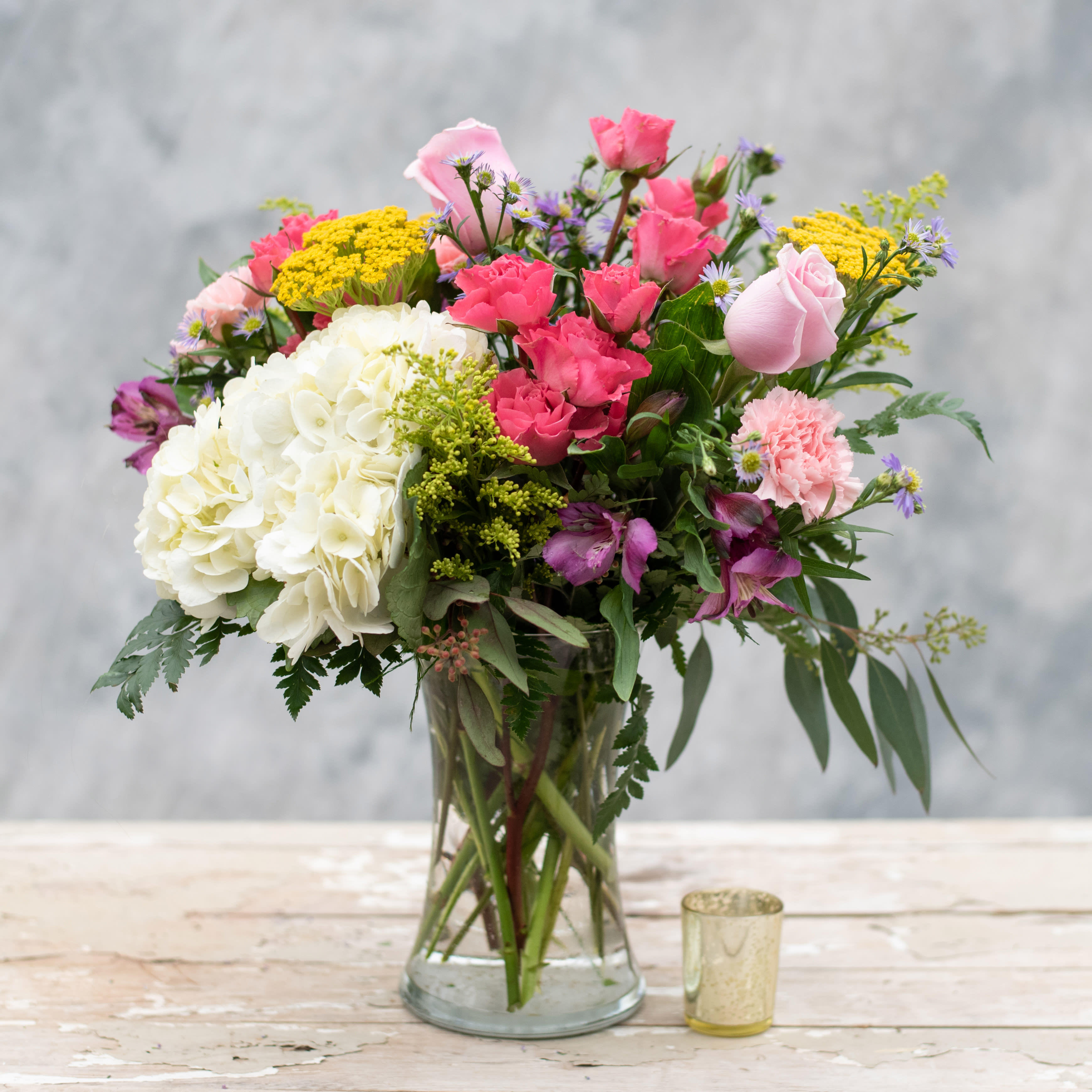Sweet Garden - Time to bring your "Sweet Garden" inside with this 8" clear gathering vase filled with the colors of spring, including pink spray roses, purple alstroemeria, pink carnations, white hydrangea, yarrow and more.  