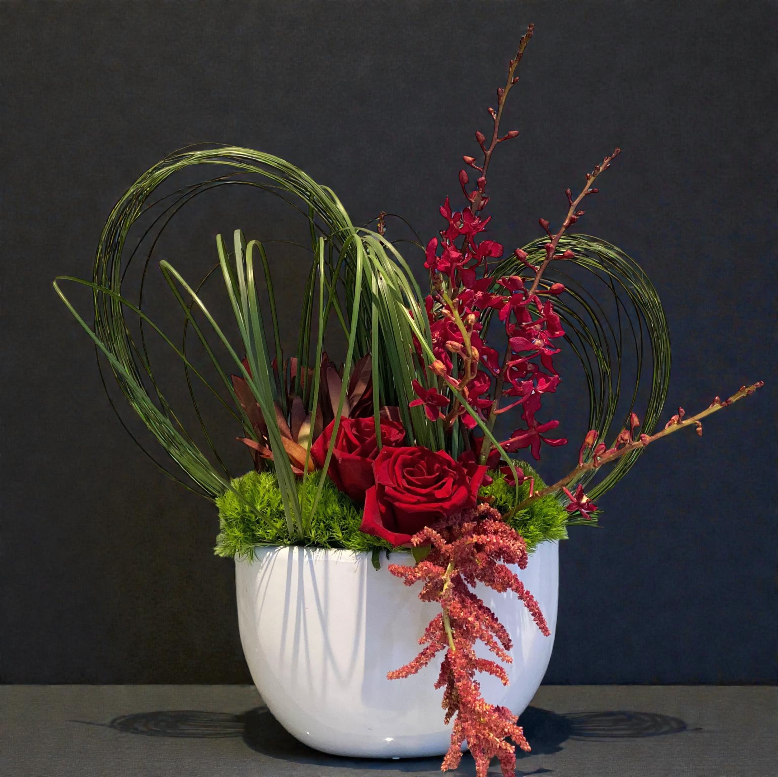 #44 My Heart Flutters When I'm with You - Bringing the magic of the heart in this arrangement using flowers and materials known for their longevity.  Designed with stylish grass shapes, gorgeous Heart Roses, and exceptional orchid stems, this display of love is unique. Ceramic container measures approximately 12"x6"