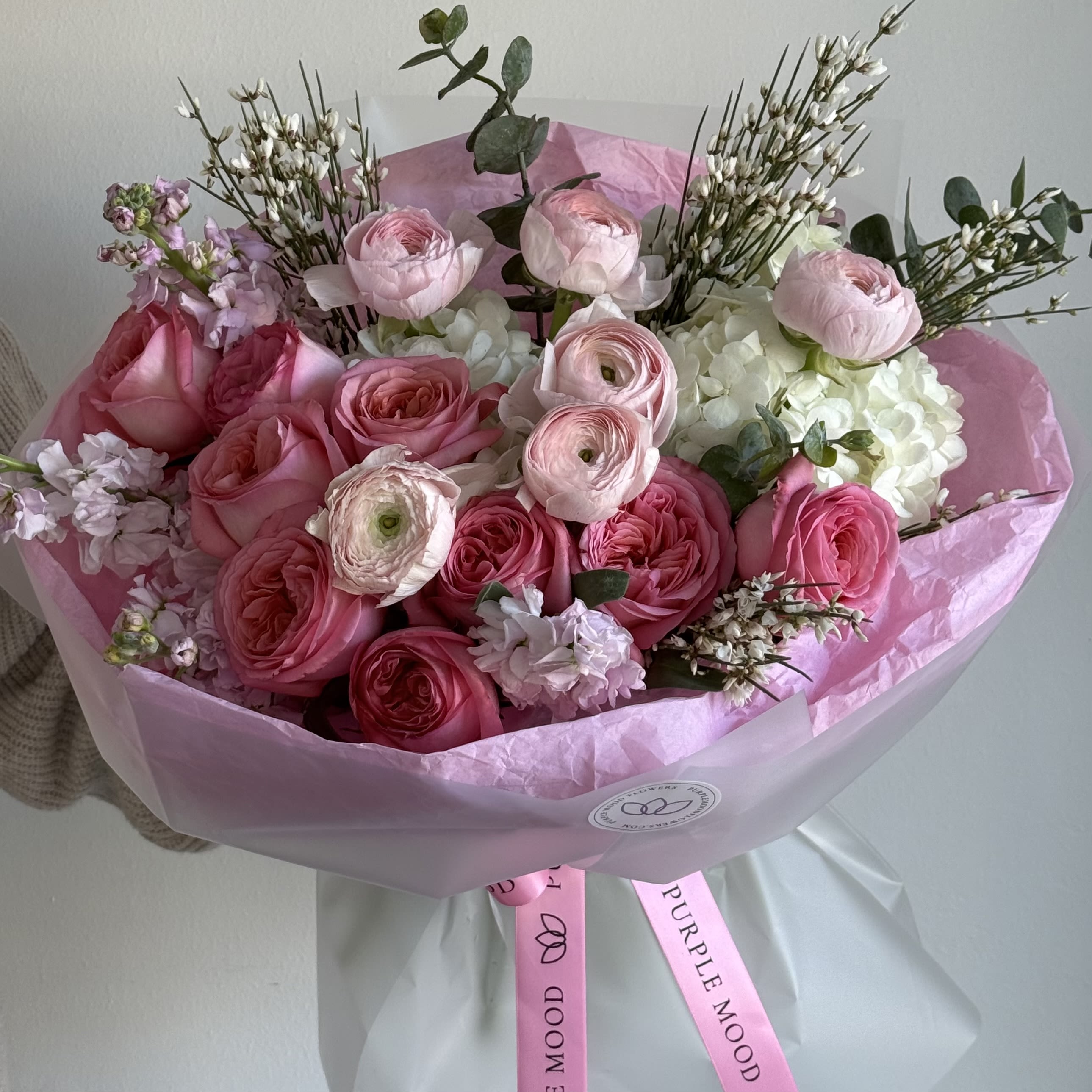 Love in Bloom Bouquet - Soft, romantic, and irresistibly elegant — Love in Bloom is a luxurious Valentine’s bouquet designed to express pure affection through layers of delicate pink blooms, creamy whites, and airy textures. This arrangement features premium garden roses, ranunculus, hydrangea, and seasonal florals, thoughtfully composed to feel both abundant and refined.  Each bouquet is hand-crafted with attention to every detail, creating a dreamy, couture-style floral statement perfect for Valentine’s Day, anniversaries, or romantic surprises.  Important details: • This bouquet is delivered without a vase and comes beautifully wrapped in our signature Purple Mood packaging. • Available in three sizes:  Standard, Deluxe, and Premium — the larger the size, the more flowers and the fuller, more luxurious the bouquet will be. • The bouquet shown in the photo is the Standard size.  Please note that while we always maintain the same color palette and overall style, flower varieties may vary slightly depending on seasonal availability, ensuring the freshest and most beautiful result every time. 