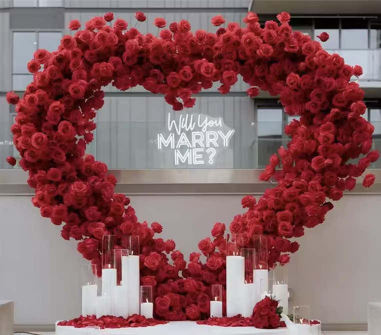  “Will You Marry Me?” Luxury Proposal Setup  - Create an unforgettable moment with our “Will You Marry Me?” Luxury Proposal Setup — a breathtaking heart-shaped floral arch overflowing with lush red roses, complemented by glowing candles and a modern neon sign. This romantic arrangement sets the perfect backdrop for your proposal, blending elegance and emotion in one stunning display.  Perfect for: rooftop proposals, private dinners, engagement parties, and luxury events.   Includes:     •    Custom heart-shaped red rose arch (8' tall)     •    “Will You Marry Me?” LED neon sign     •    Elegant candle display with glass cylinders (12 pieces)     •    Floor petals around candles for a complete romantic ambiance     •    Setup, delivery + pick up NYC &amp; Nassau County Area  *** Please call our store to coordinate date and time availability.        718-954-3044.   