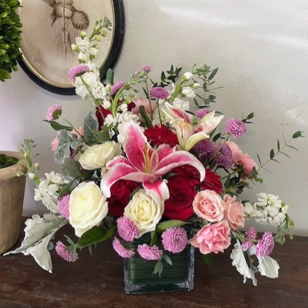 Sweetest Love - The arrangement is naturally stylized, with touches of blossomy flowers added for a touch of sweetness. Florals such as fragrant stock, roses, scabiosa, ranunculus, petite roses, large roses, and gerberas with soft foliage are featured. -STANDARD shown 22”h x 18”w