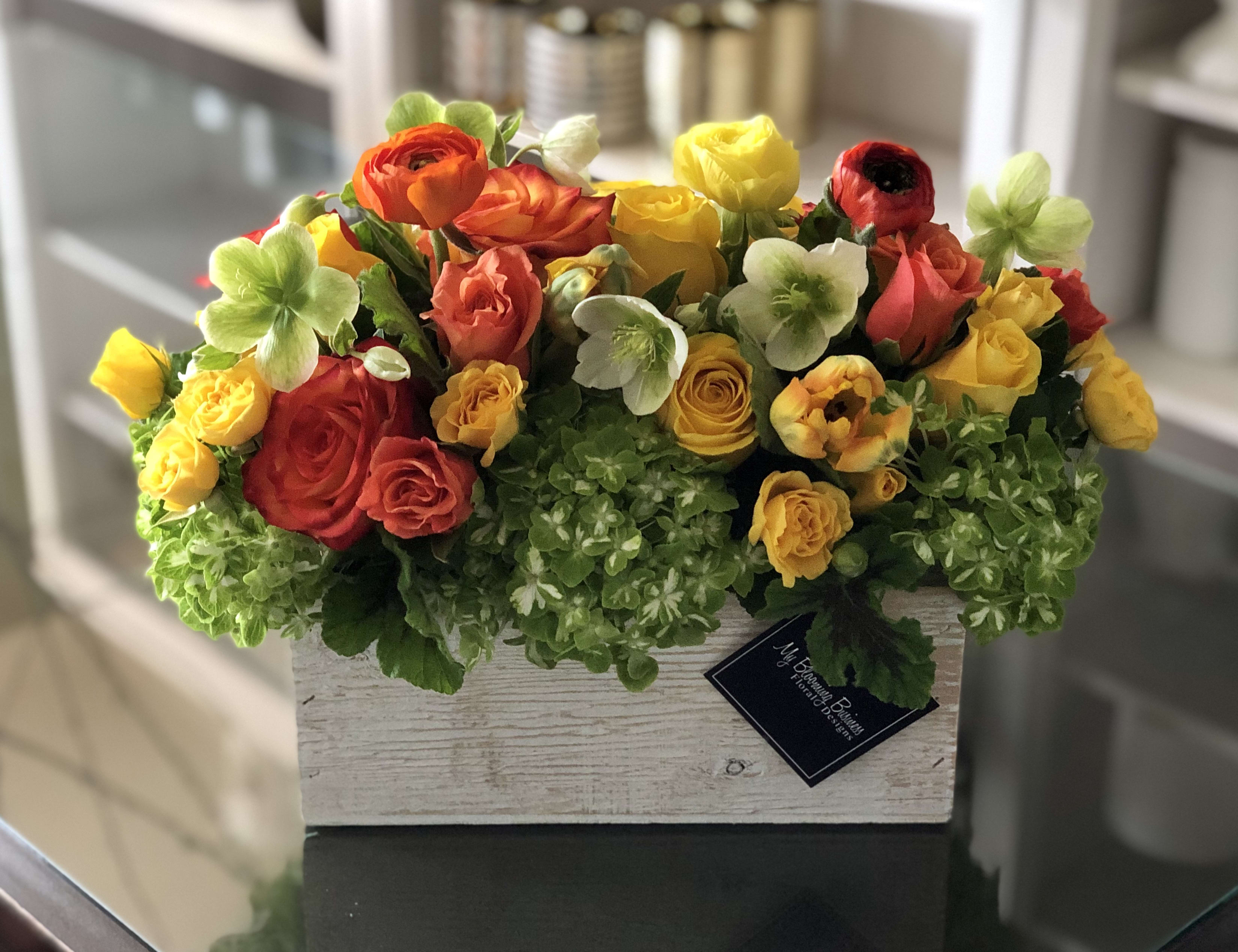 Walking on Sunshine  - Imagine a charming white wash wood box filled to the brim with delicate green hydrangeas, vibrant yellow and orange florals resembling the warmth of a sunrise, and a medley of other premium seasonal flowers, all hand-picked and arranged with love. It's like stepping into a whimsical garden right in the comfort of your own home. 