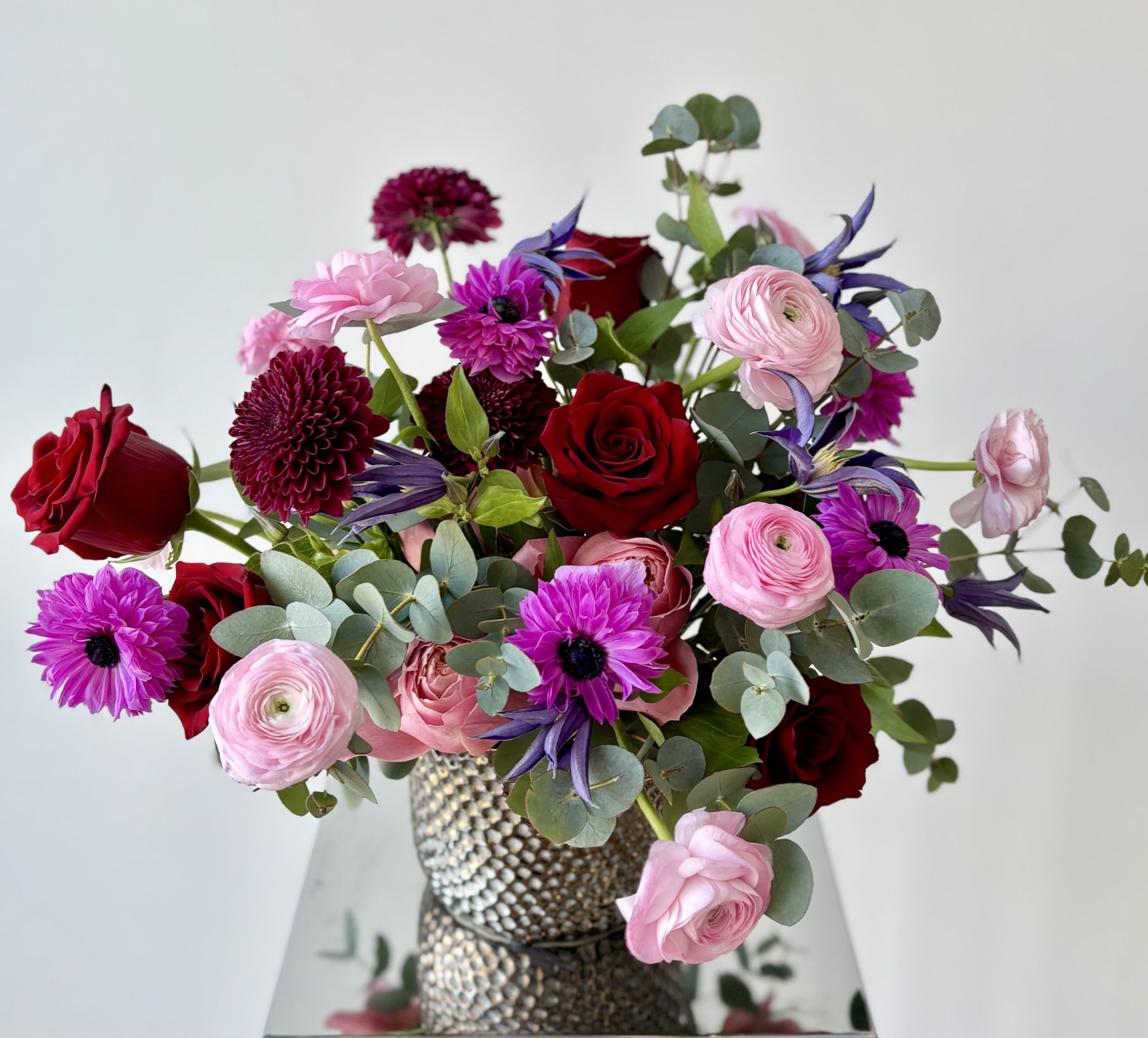 J'Adore - Elegant Valentine's Day flower arrangement of premium red roses, red/burgundy cremons and pink ranunculus with a pop of fuchsia anemones and purple clematis with beautiful silver green foliage of eucalyptus. 