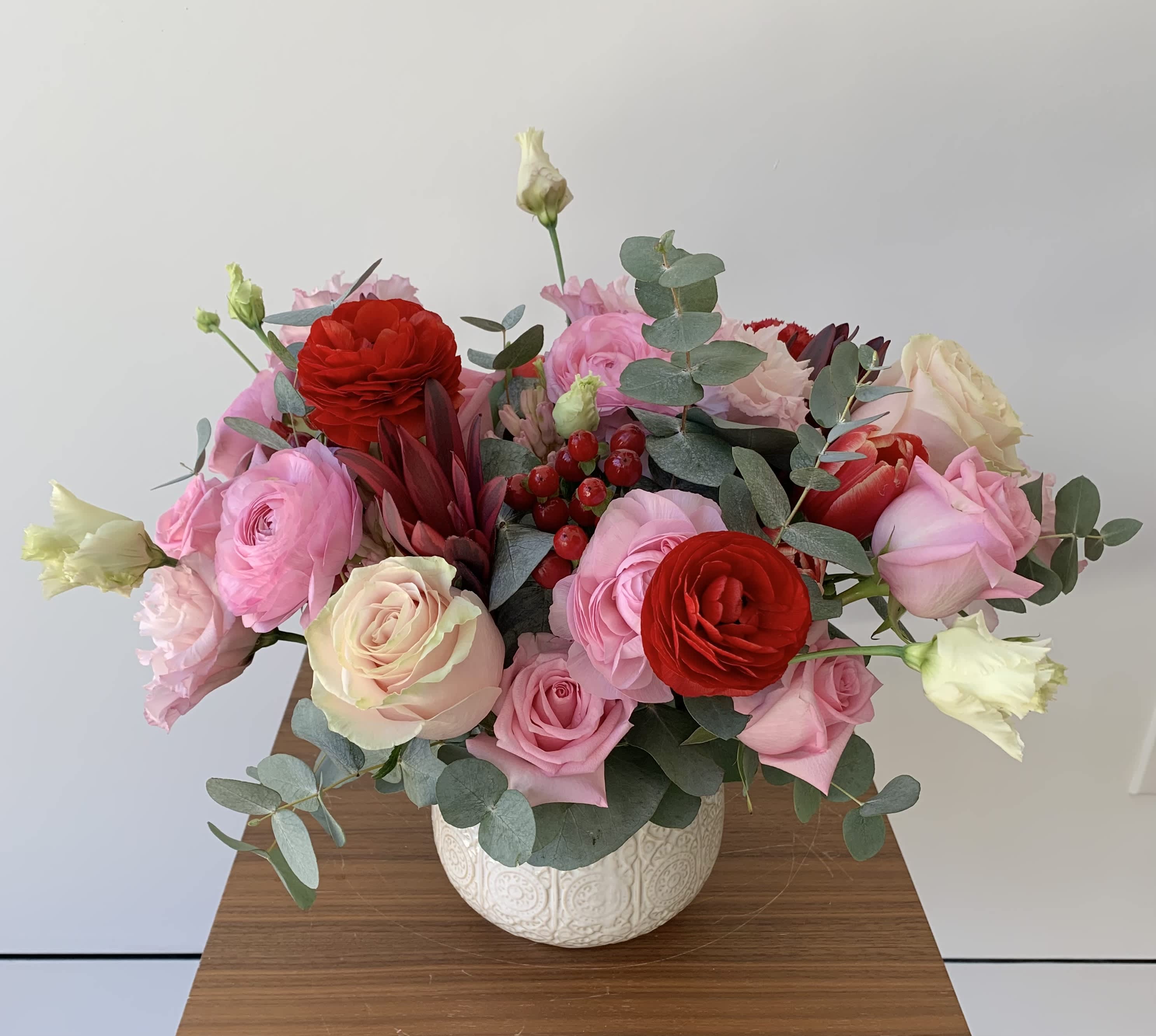 Love in Bloom - An elegant flower arrangement of premium red and pink blooms nestled in eucalyptus stems. The flower mix usually has roses, lisianthus, ranunculus, tulips, hyacinths, red hypericum and additional fillers. 