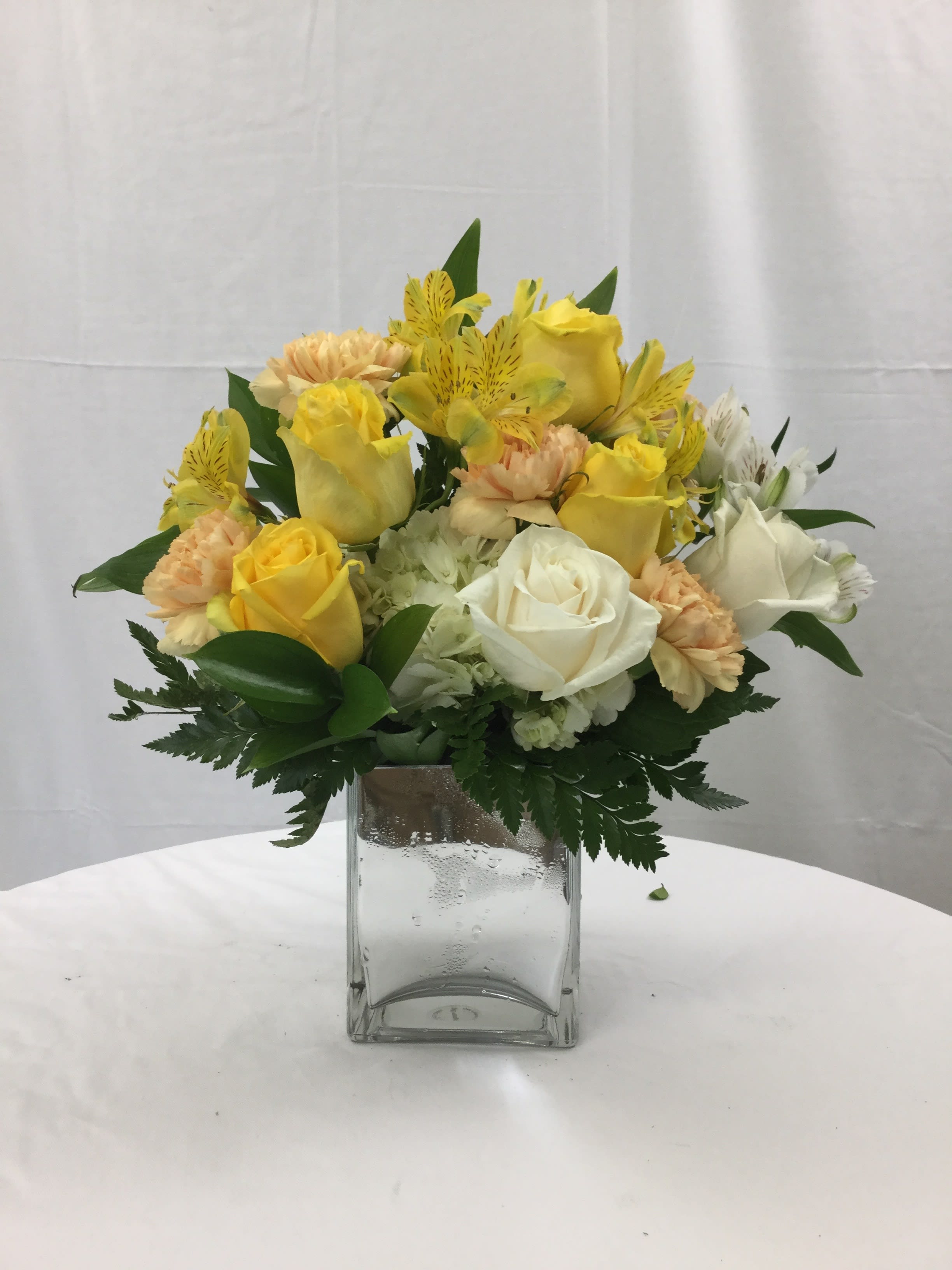 Bouquet of Cheer Bouquet - This beautiful bouquet is full of fresh yellow, white and even peach blooms. It is handcrafted and designed in a clear glass cube. It makes for a wonderful gift for every special occasion, including parties as a table centerpiece!
