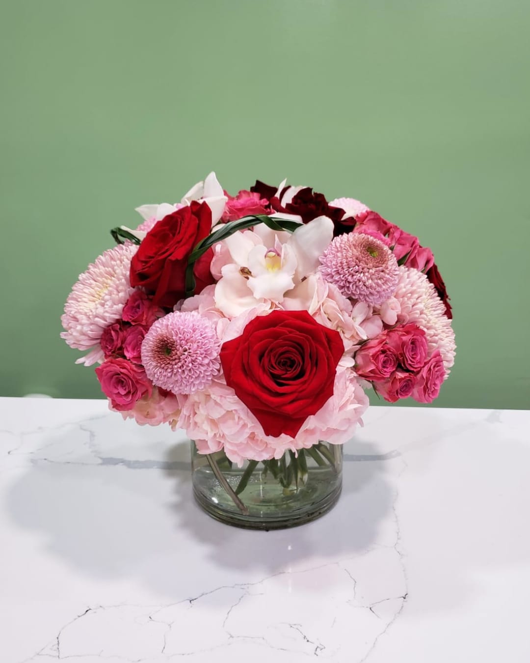Sparkling Rosé  - This fabulous arrangement has hydrangeas, roses, spray roses, cymbidium, cremons, and bear grass in a clear cylinder vase. 