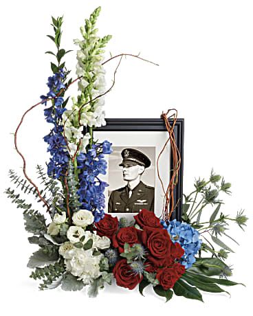 Always With Us Photo Tribute - Honor the memory of an always-beloved with this beautiful display bouquet. Designed to surround a favorite photo, its patriotic mix of blue hydrangea with red and white roses is a respectful tribute. This bouquet features blue hydrangea, red roses, red spray roses, white spray roses, white carnations, blue delphinium, white snapdragons, blue eryngium, dusty miller, curly willow, spiral eucalyptus, parvifolia eucalyptus, aralia leaf and lemon leaf. Arrangement does not include photo and/or picture frame. Approximately 22 1/2" W x 25 1/2" H