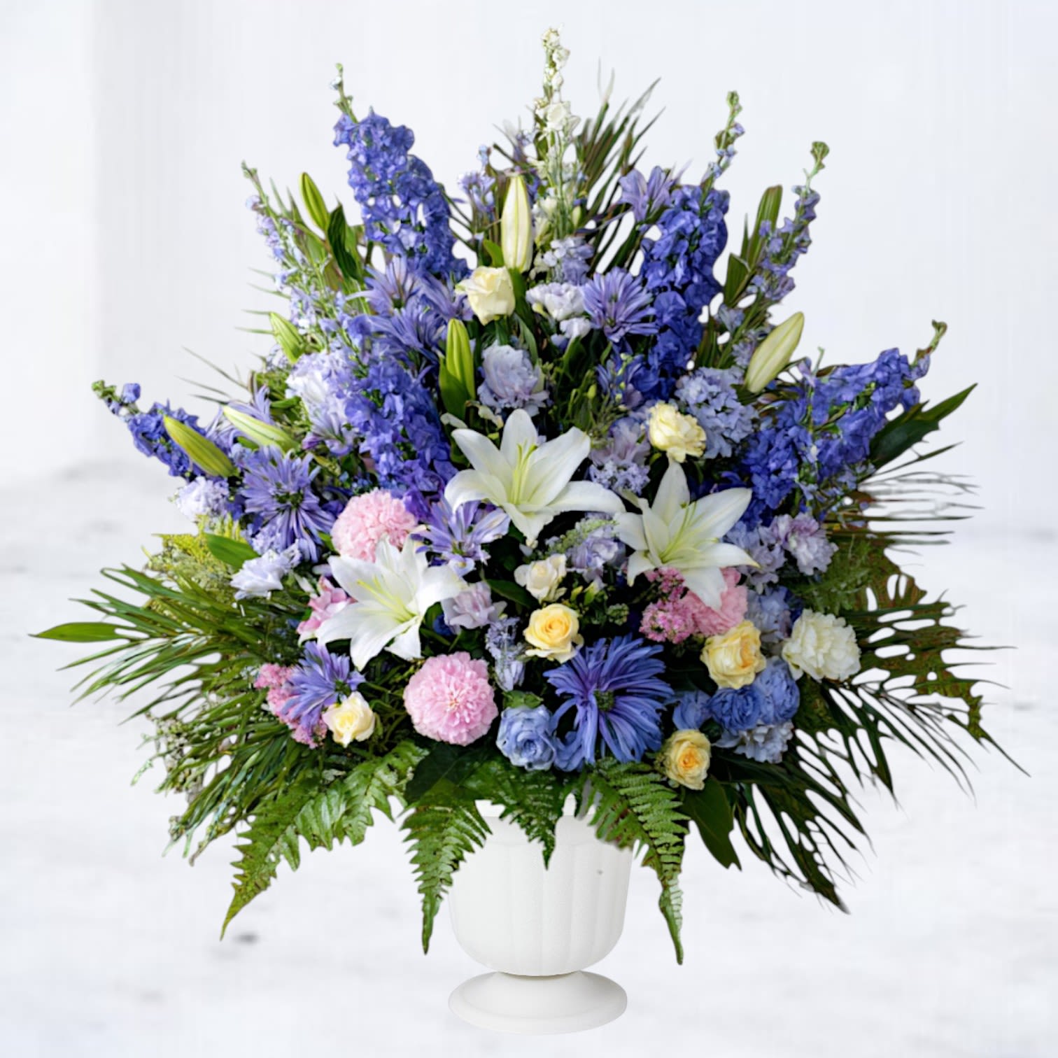 Aurelian - Aurelian is a graceful funeral service arrangement composed in calming tones of blue, lavender, soft ivory, and fresh greenery. Flowing textures and layered blooms create a sense of movement and quiet strength, offering comfort while honoring memory with elegance and care.  Designed in a classic urn-style vessel, Aurelian is well suited for memorial services and celebrations of life, providing a serene yet expressive tribute that feels both thoughtful and enduring.