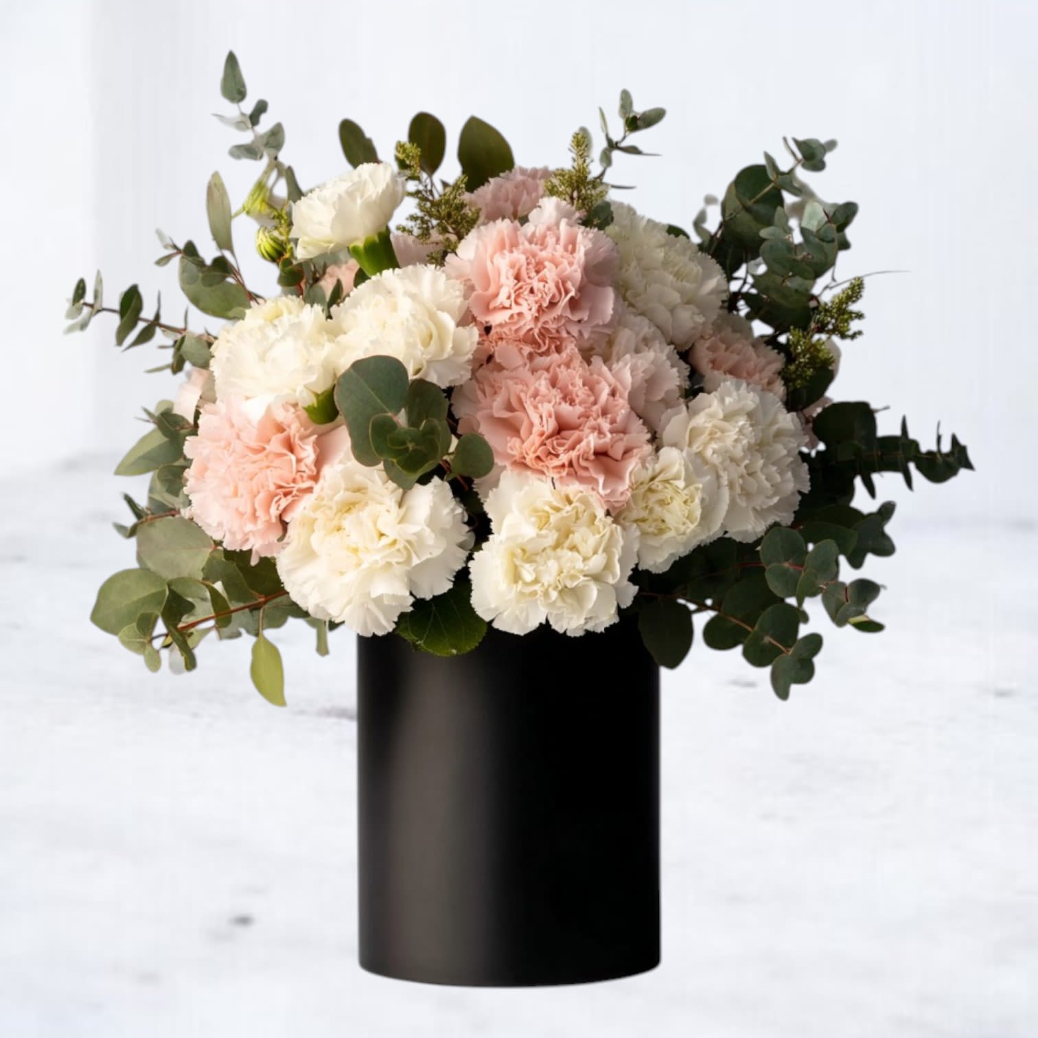 Blush Noir Bouquet - The Blush Noir Bouquet brings timeless romance into the modern era with a striking mix of delicate pink and white carnations set against lush eucalyptus greenery. Designed in a bold matte black vase, this floral arrangement is perfect for those who love soft, feminine blooms with a contemporary edge. Ideal for birthdays, anniversaries, sympathy gestures, or simply brightening someone’s day, this chic bouquet adds elegance to any space.  Whether you’re sending flowers across Houston, Magnolia, The Woodlands, or surrounding areas, this arrangement delivers both heartfelt sentiment and standout style.