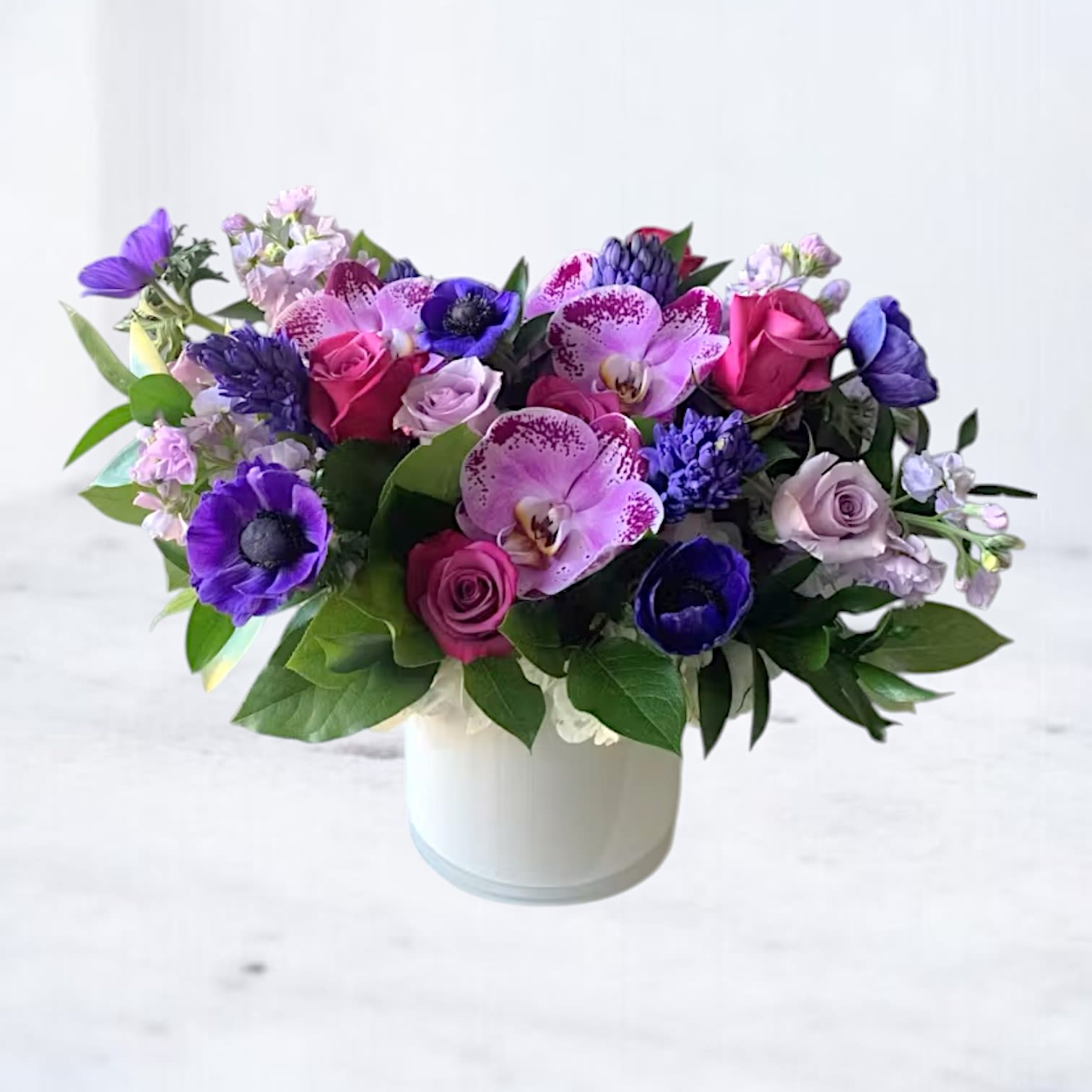 Velvet Twilight - Honor a loved one’s memory with the Velvet Twilight arrangement, a striking and elegant floral tribute featuring lush roses, exotic orchids, and deep-hued anemones. This sophisticated design blends rich purples, soft lavenders, and vibrant pinks to create a heartfelt expression of sympathy. Accented with delicate stock flowers and premium greenery, this arrangement conveys warmth, remembrance, and the beauty of a life well-lived. Ideal for funeral services, memorials, or as a comforting gesture to grieving families.