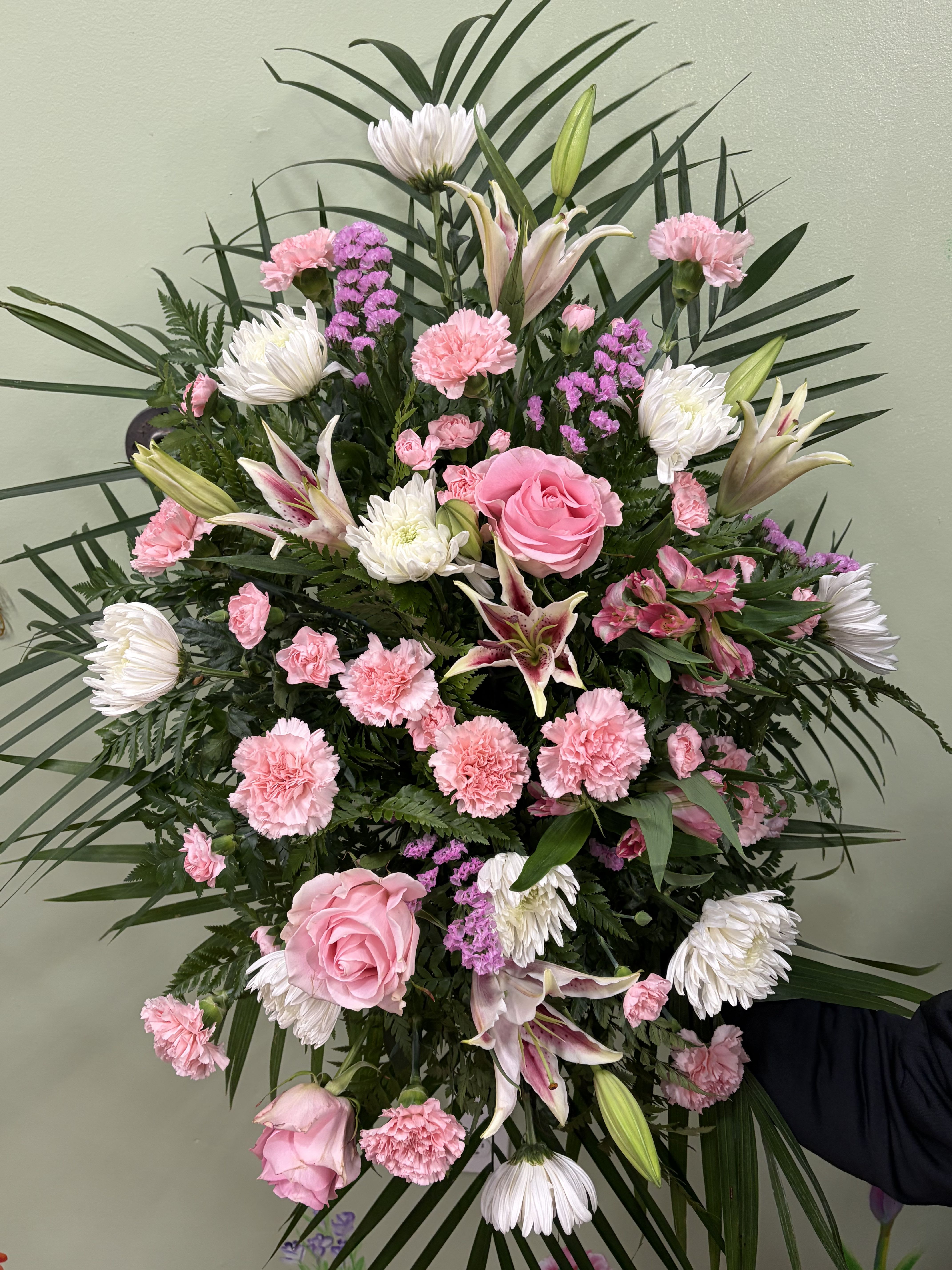 Blush Serenity Standing Spray - A graceful standing spray featuring soft pink roses, pink carnations, white chrysanthemums, and elegant lilies, accented with delicate purple filler flowers and lush greenery. Designed with height and balance, this arrangement conveys comfort, peace, and heartfelt sympathy, making it well suited for memorial services and celebrations of life.